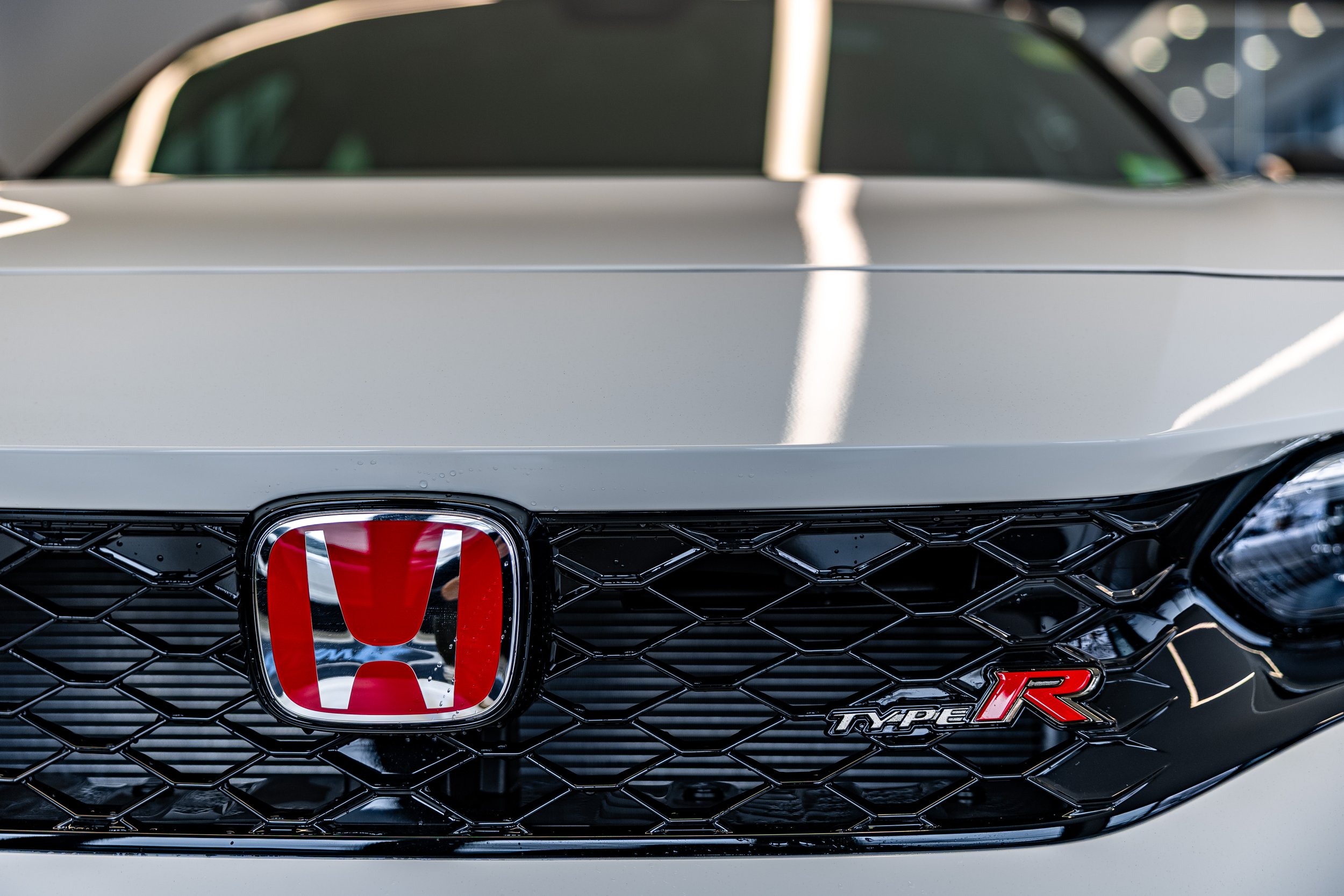 Close-up of the front of a white Honda Civic Type R, showing the Honda emblem, black grille, and Type R badge.
