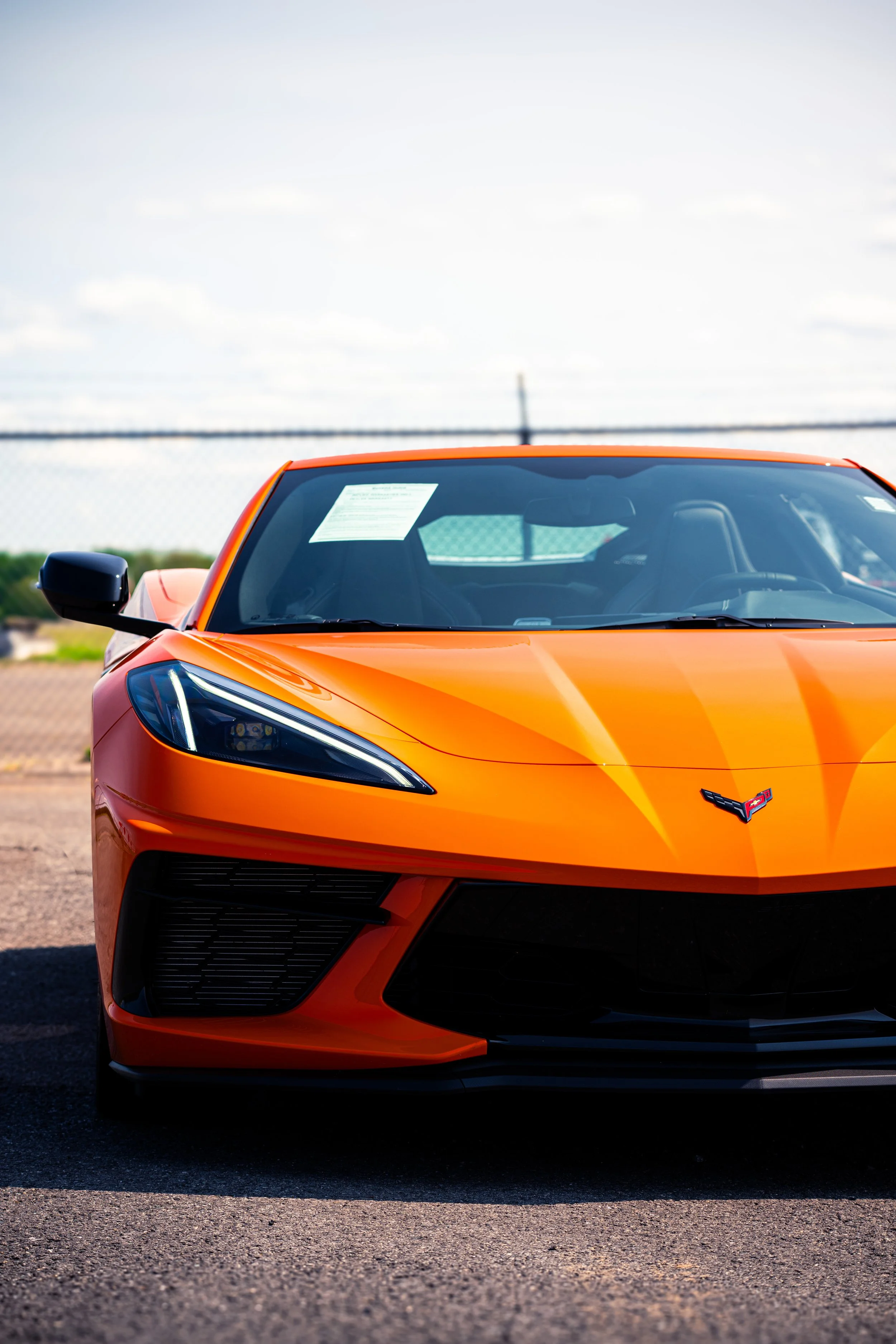 Orange Chevrolet Corvette sports car parked outdoors on asphalt with a clear sky in the background.