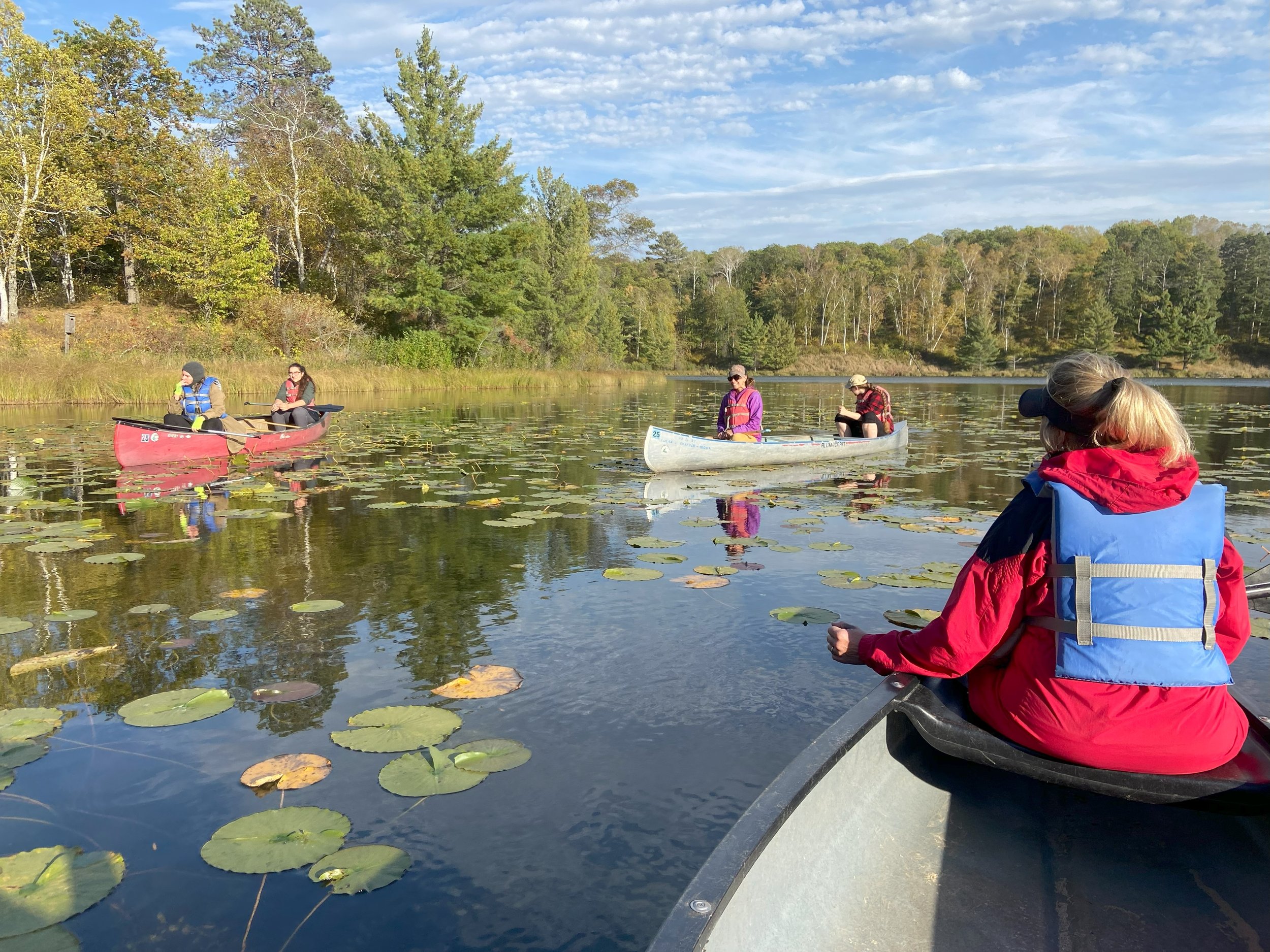 People canoeing on a peaceful lake surrounded by trees with autumn foliage.