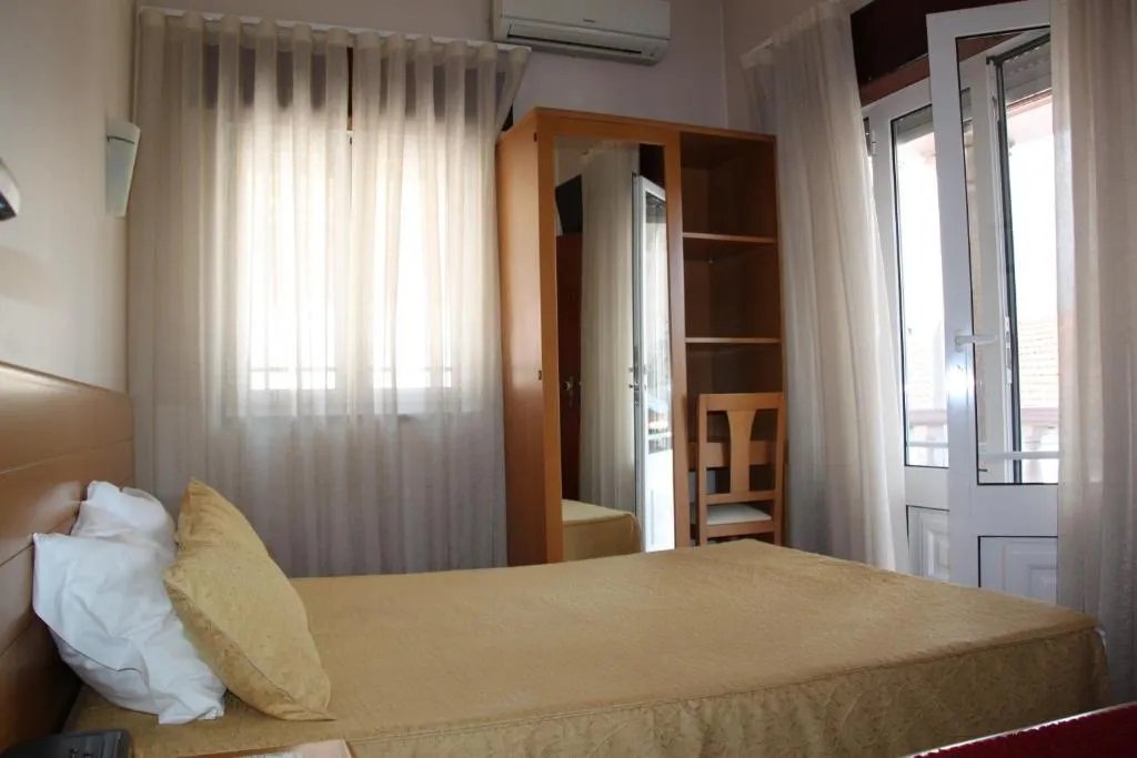 Small hotel room with single bed, window, mirror, and door to balcony.