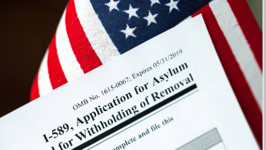 Formulario I-589 de solicitud de asilo con una bandera de Estados Unidos en segundo plano.