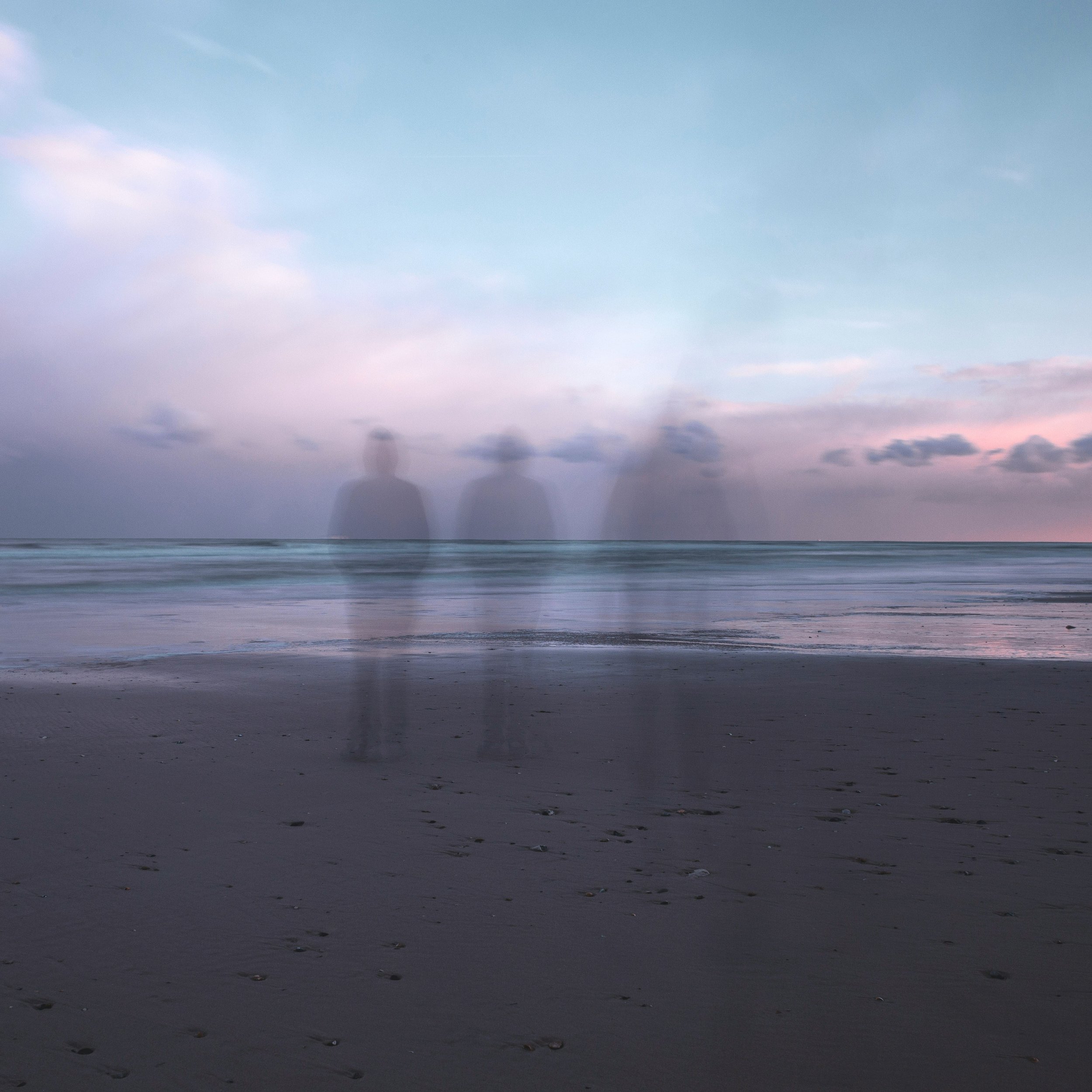 A beach at sunset with a pastel sky, and three ghostly silhouettes of people walking along the shoreline.