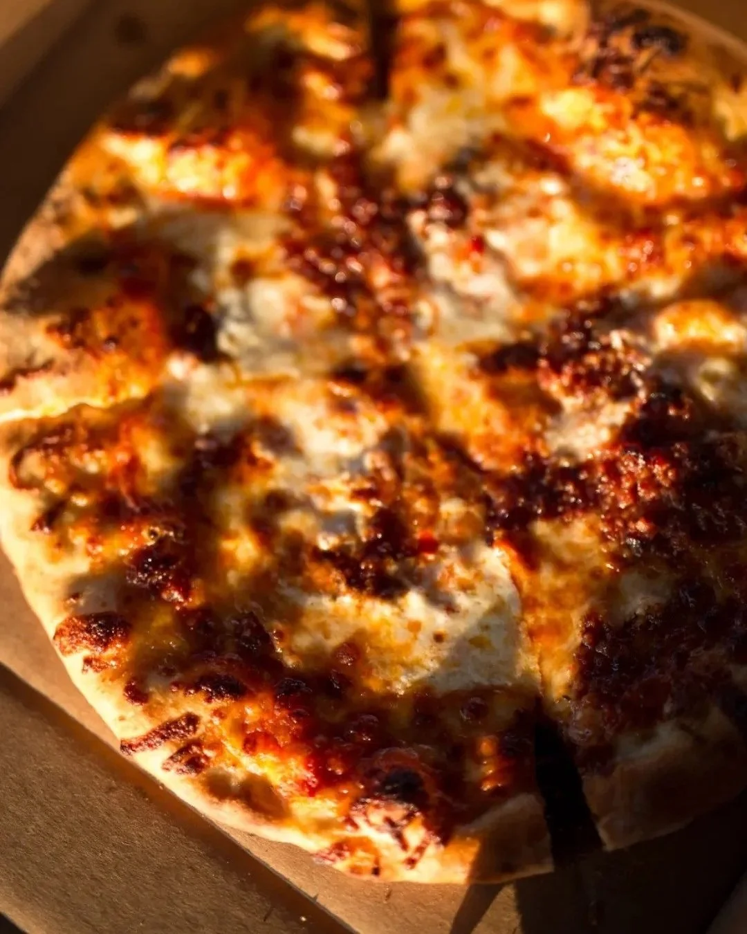Close-up of a cheese pizza with some areas slightly charred, in a cardboard pizza box.