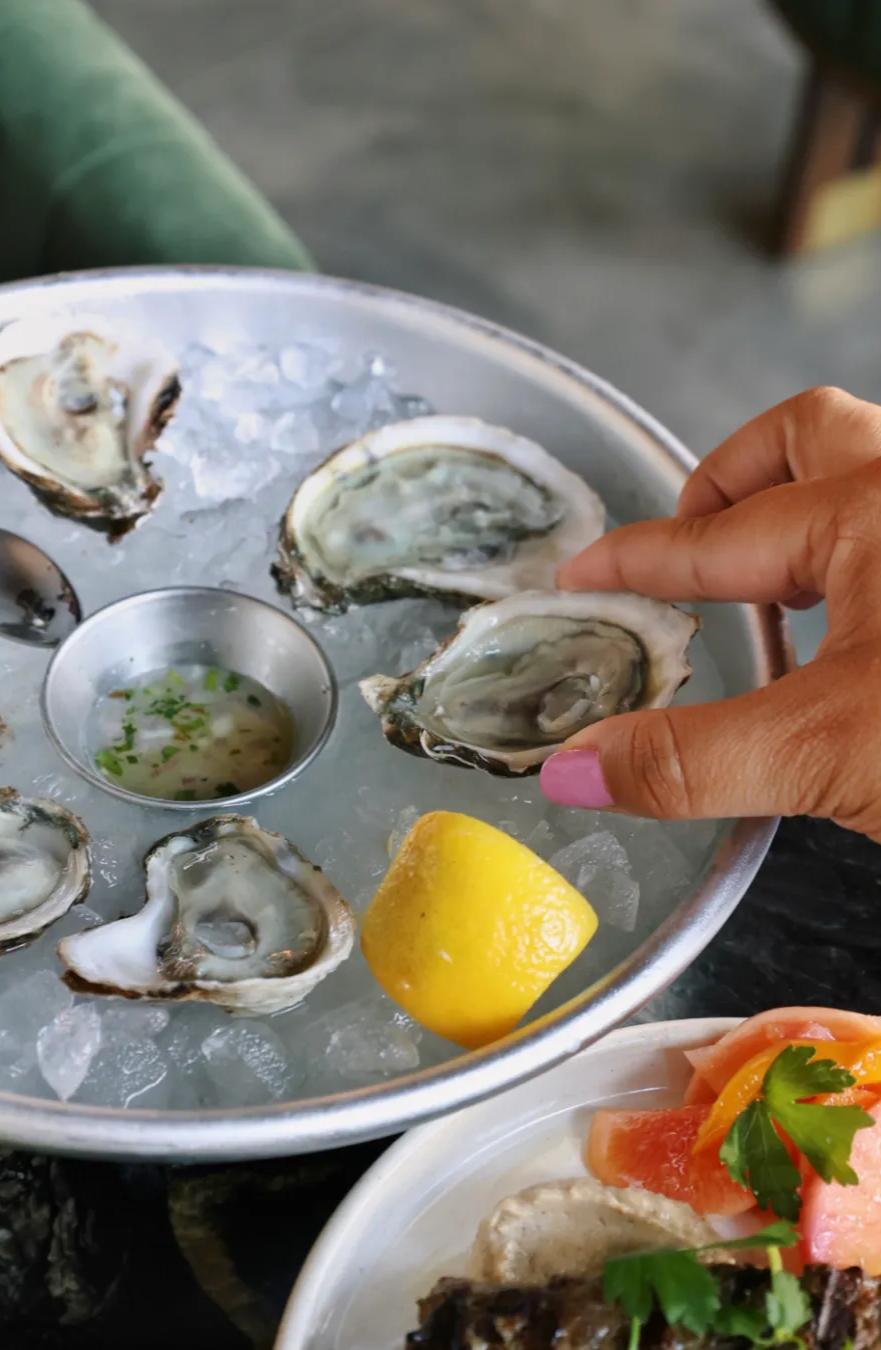 A hand grabbing fresh shucked oysters on ice, with a lemon next to it