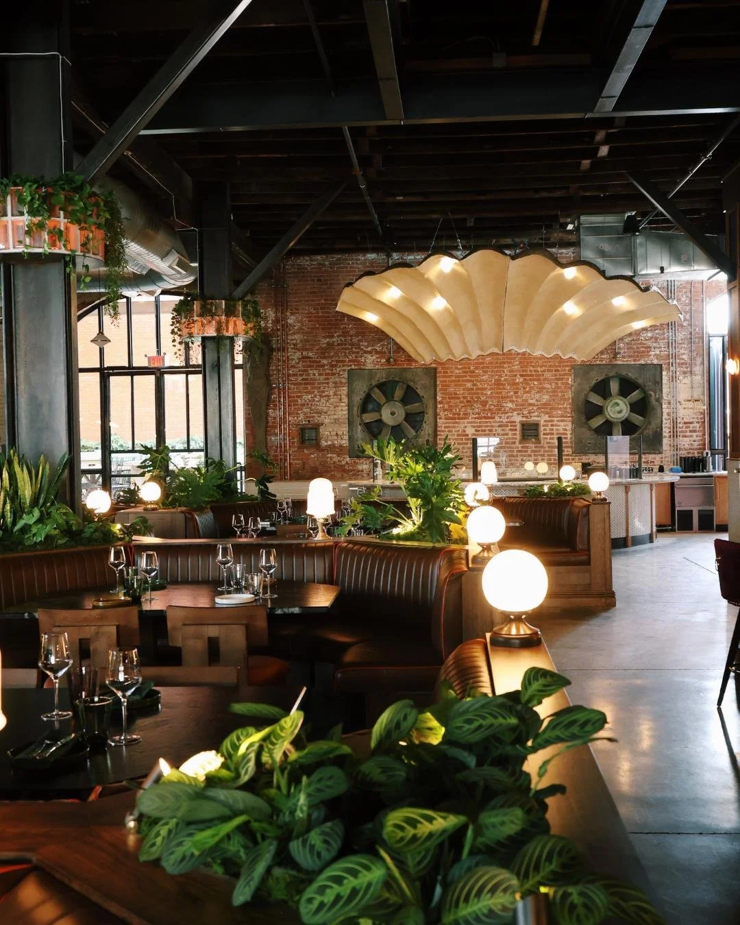 Interior of Red Herring Art-Deco inspired restaurant with dim lighting, green plants, brick walls, and decorative oyster shell-shaped light fixture.