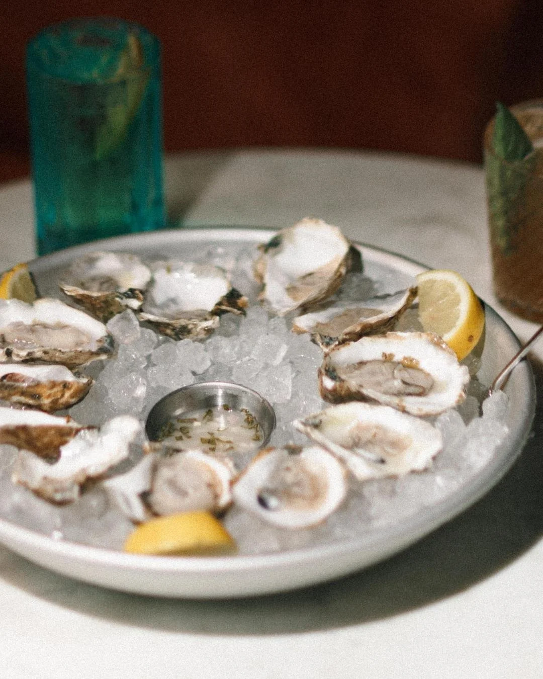 A plate of oysters and two cocktails on a white marble table