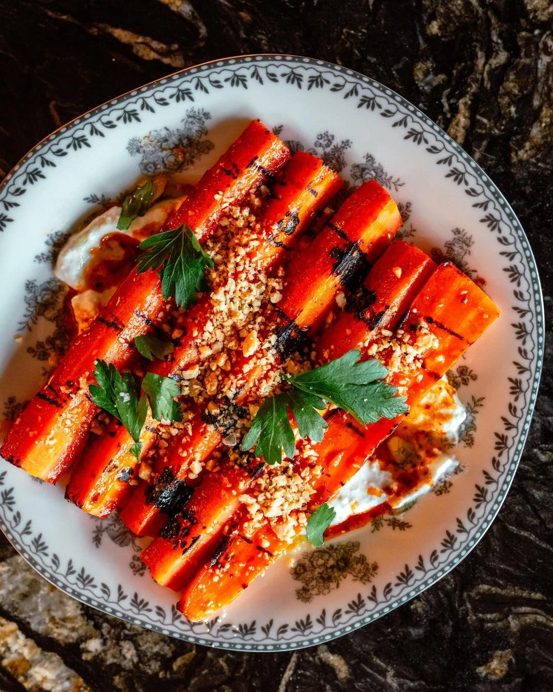 A plate of Carrots with chef prepared toppings on a black marble counter top