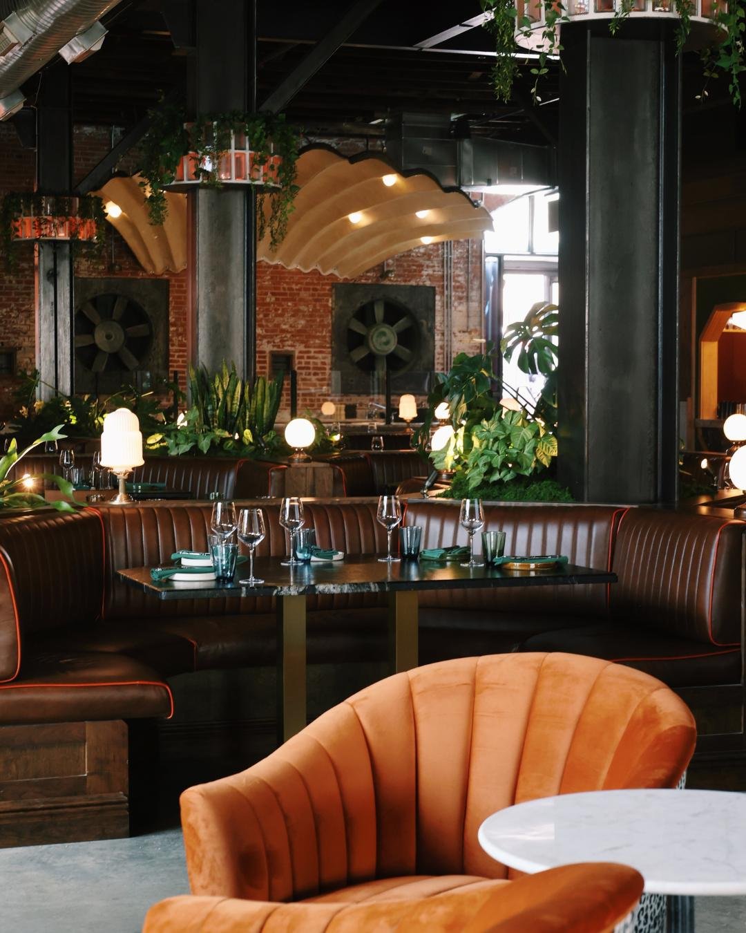 A view of the leather chairs in the booth at Red Herring Restaurant showing the Red Herring Raw bar in the background with plants and greenery throughout. 
