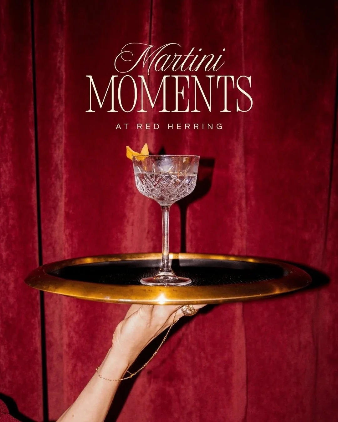 A vintage cocktail glass with a lemon twist garnish on a gold tray, held by a gloved hand against a red velvet curtain, with the text 'Martini Moments at Red Herring' above.