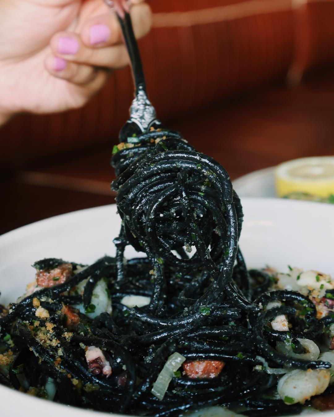 Squid Ink Pasta wrapped around a work over the plate with a hand holding the fork
