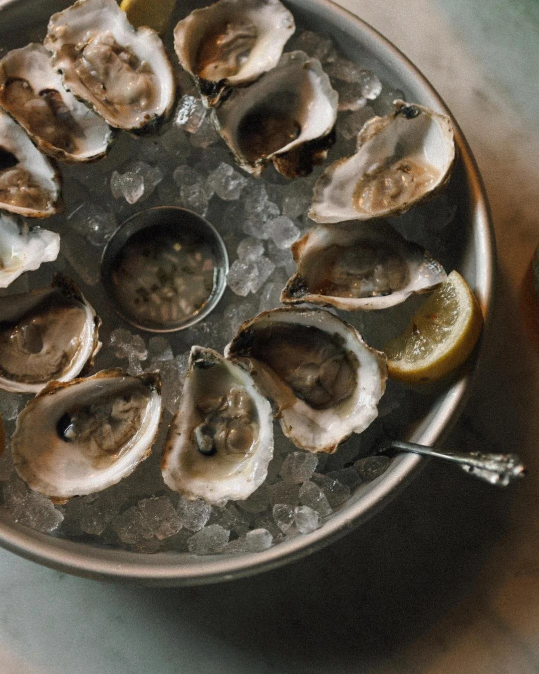 A plate of raw oysters and a cocktail sit in a dimly lit setting 