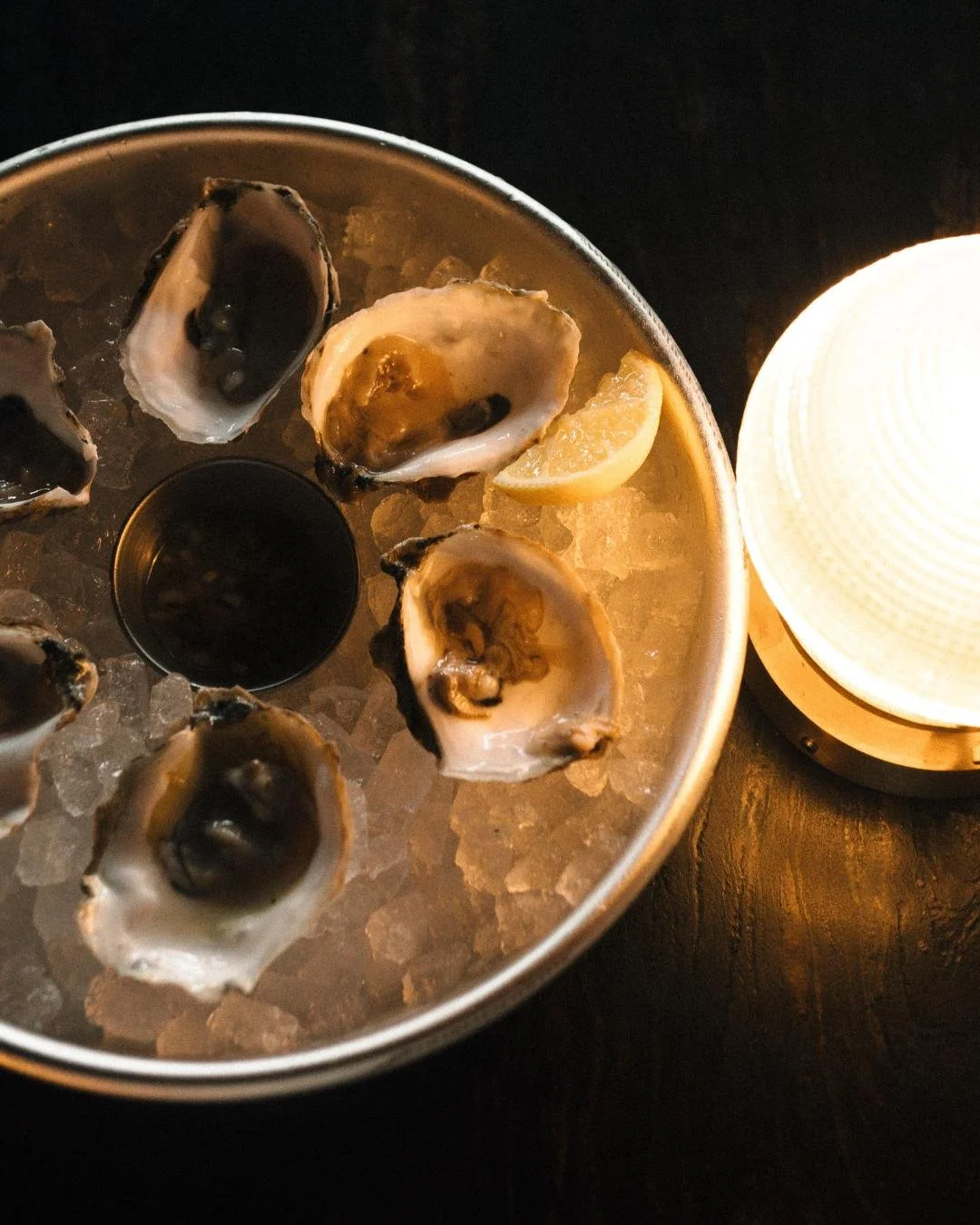 Raw oysters at Red Herring Restaurant with a coaster that says Red Herring and a circle table light that is dimly lit