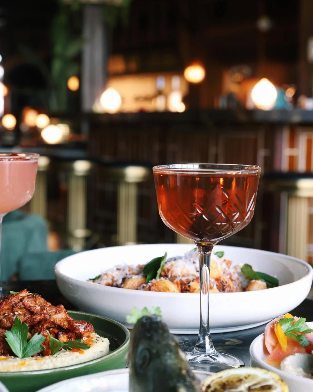 a cocktail in the middle of a table with several dishes in it.