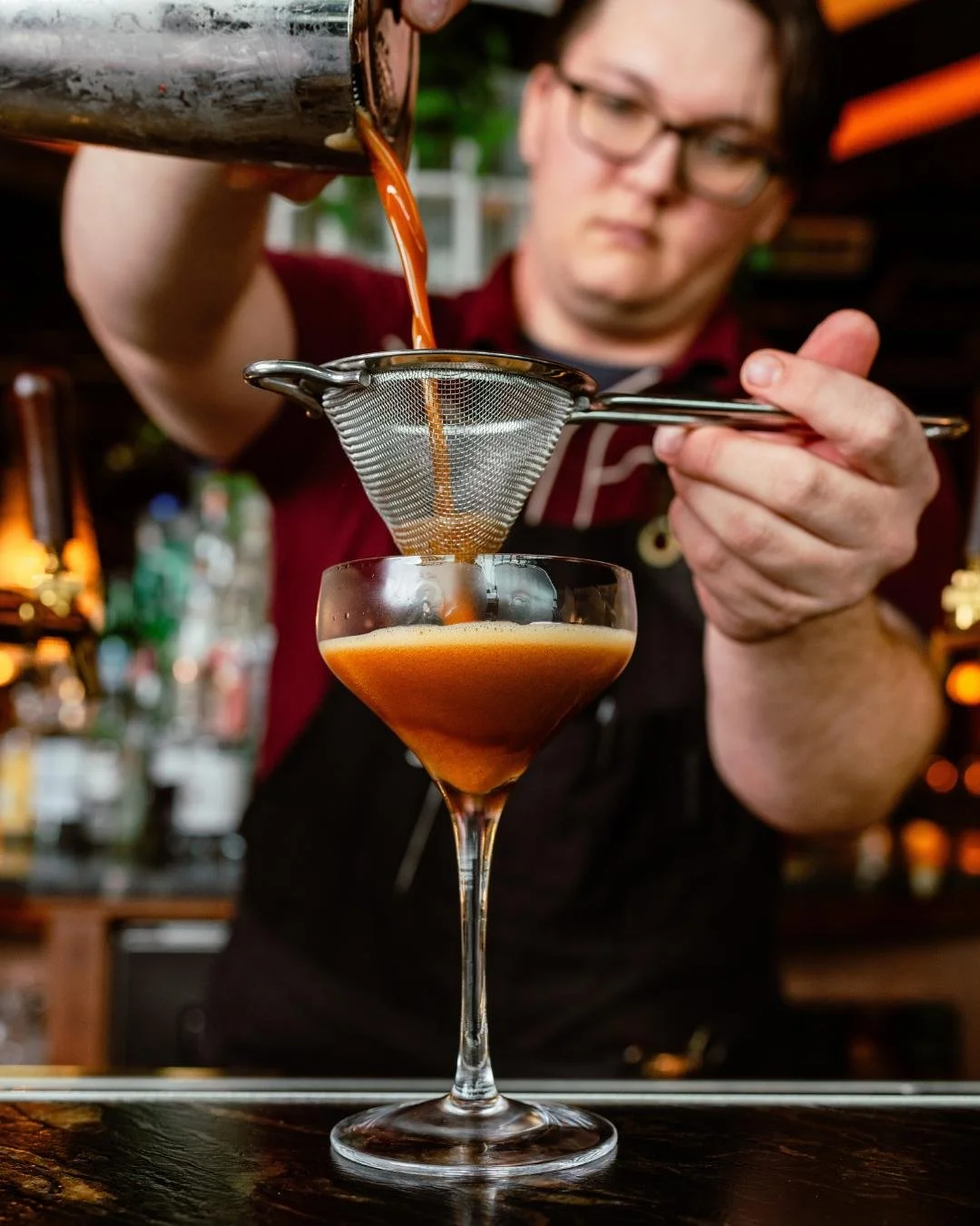 A cocktail being strained and poured by a bar tender at Red herring 