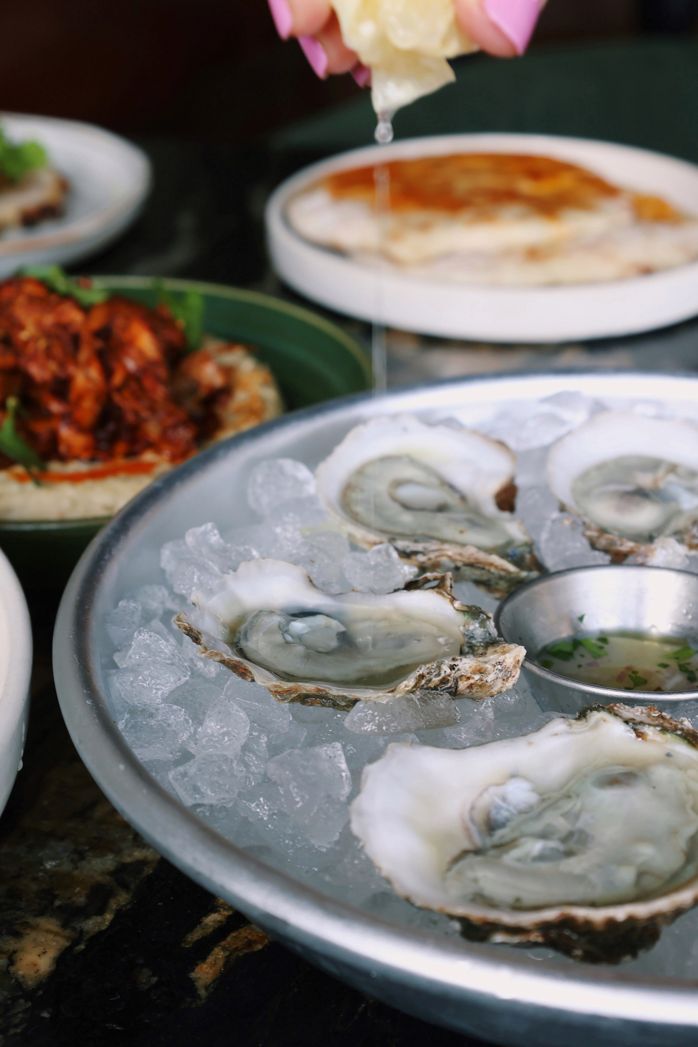A hand squeezing a fresh lemon on top of the hand-shucked oysters at Red Herring's Raw Bar