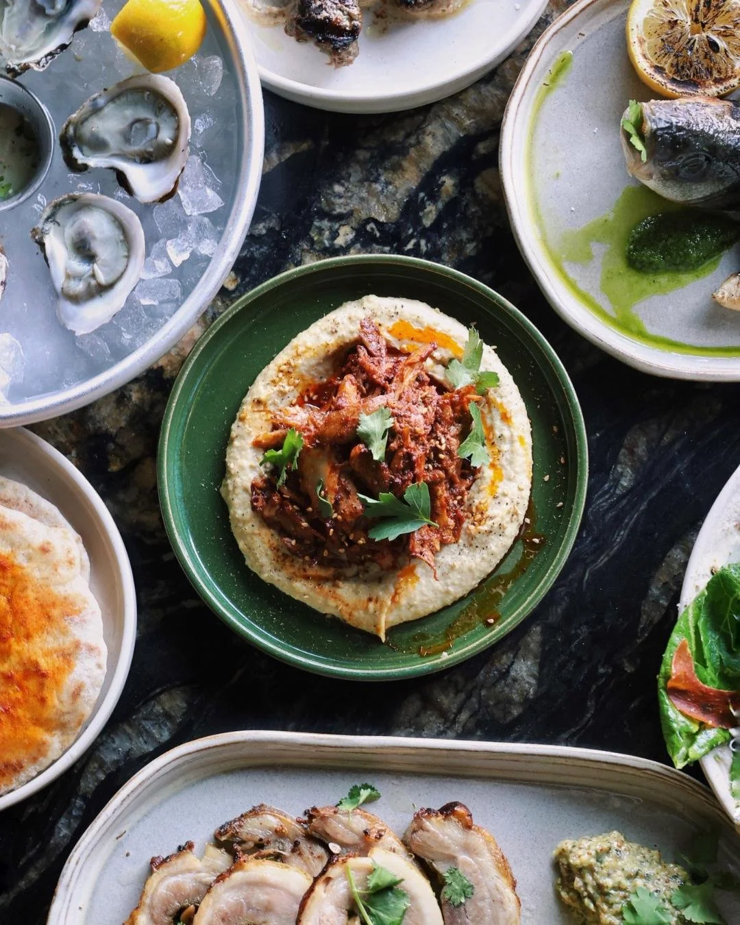 A table spread of oysters and seasonal dishes at Red Herring restaurant with a black marble counter top behind 