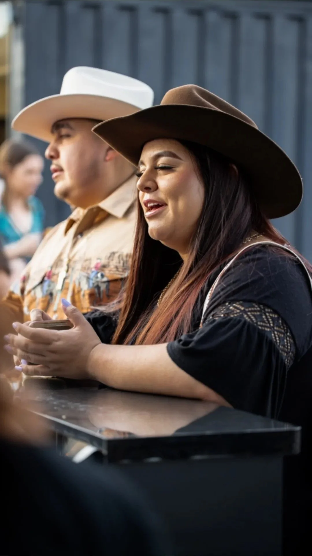 People wearing cowboy hats, including a woman with a brown hat and a man with a white hat, sitting at a table.