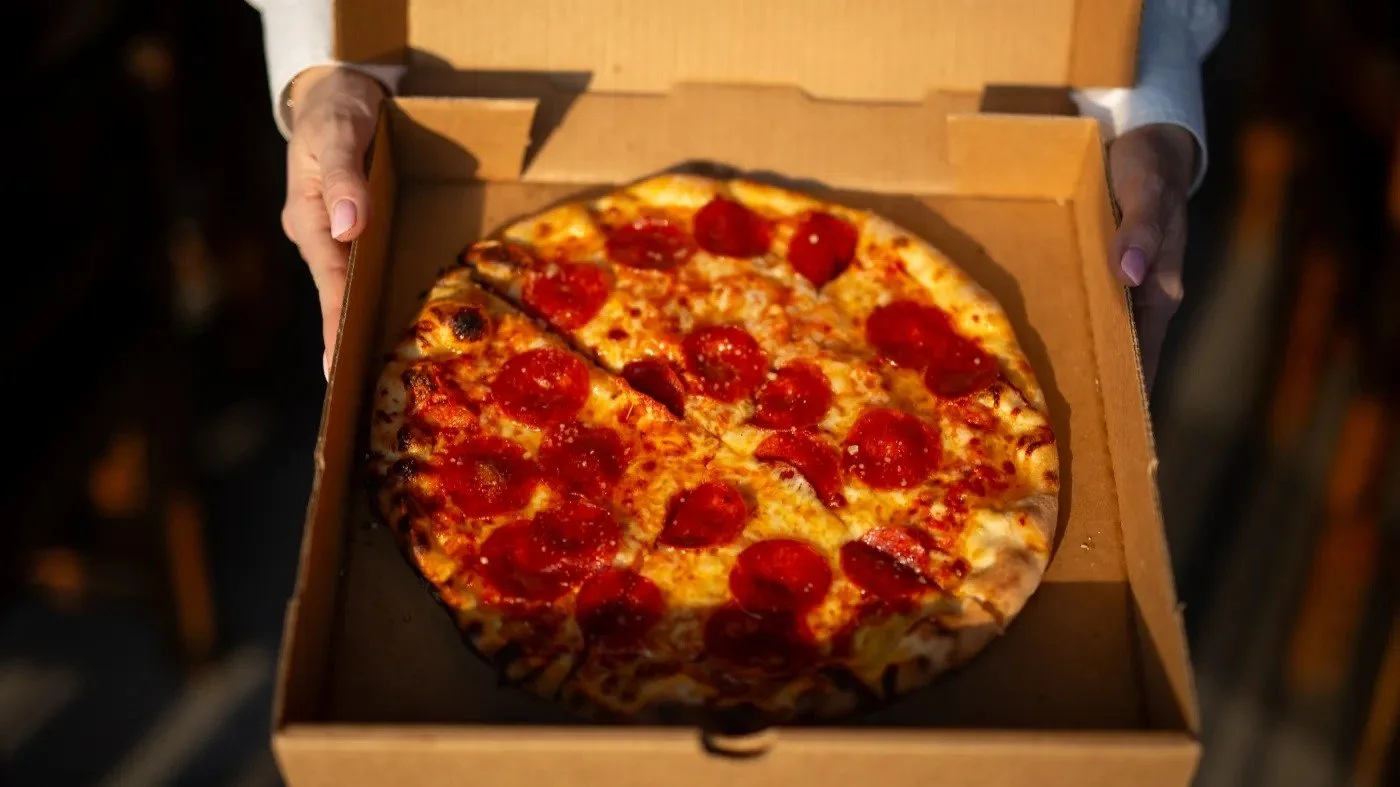 Person holding a cardboard box with a pepperoni pizza inside.