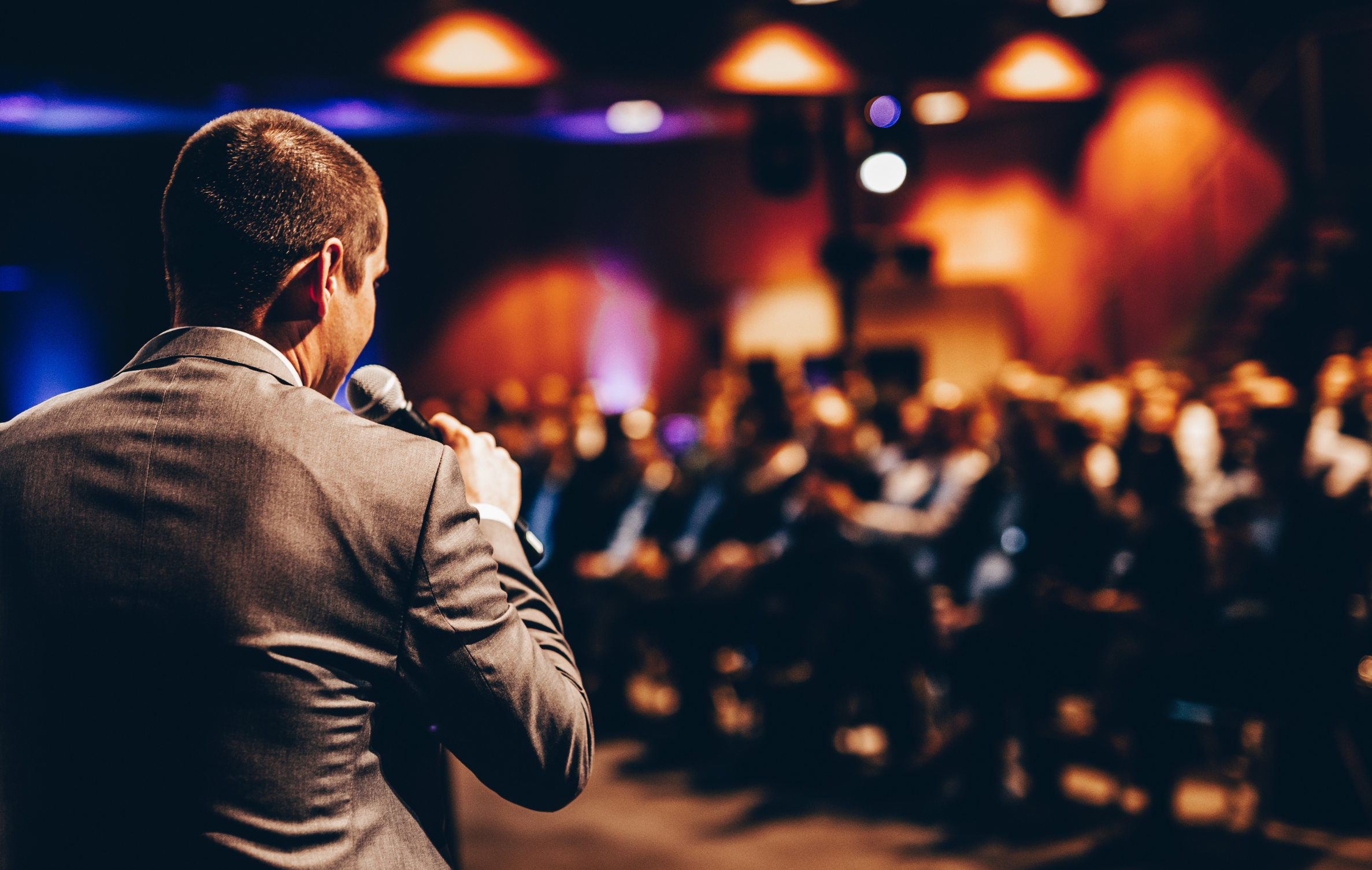Speaker in suit with microphone facing audience at conference.