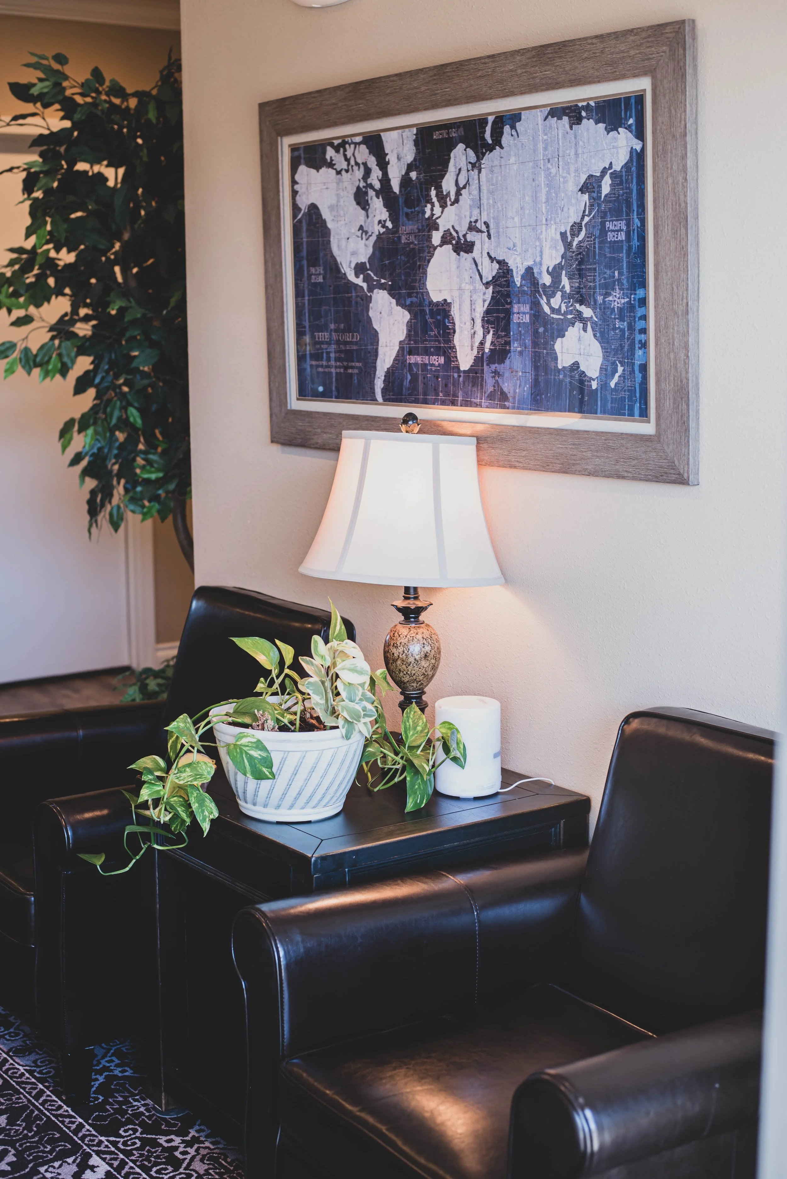 Living room or office corner with a black table, a potted plant, a table lamp, and a framed world map on the wall.