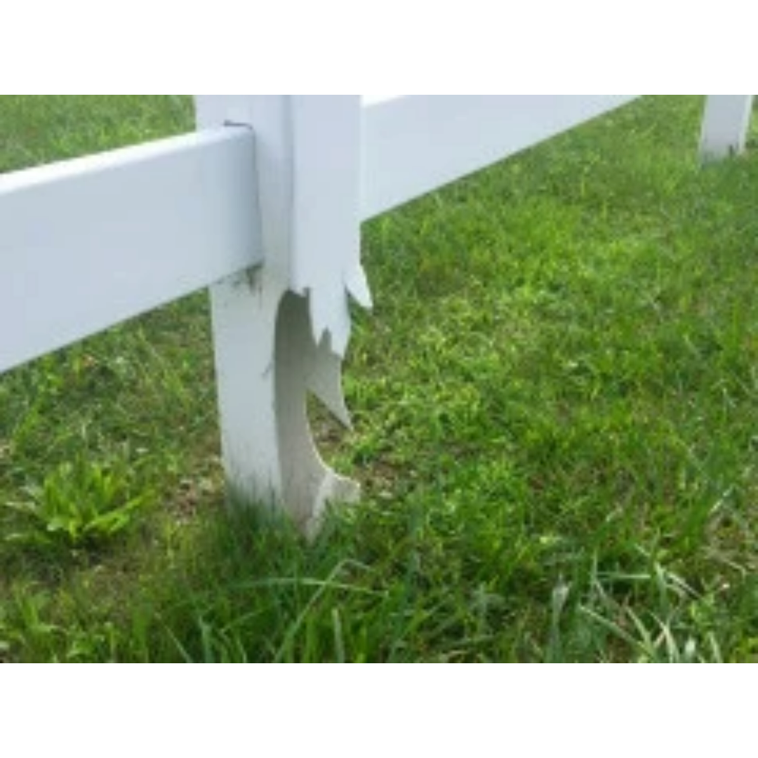 Close-up of damaged white wooden fence post with broken paint, on green grass.