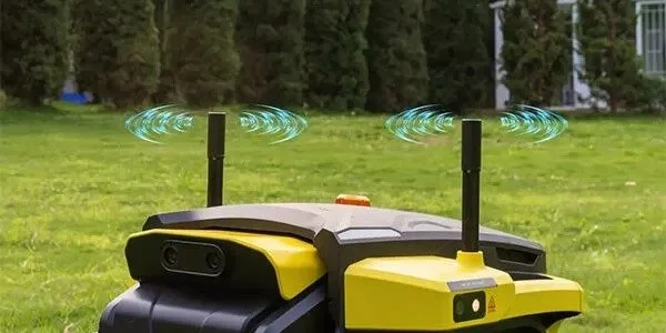 A yellow and black robotic lawn mower with two tall antennas emitting signals, on a grassy lawn with trees and bushes in the background.