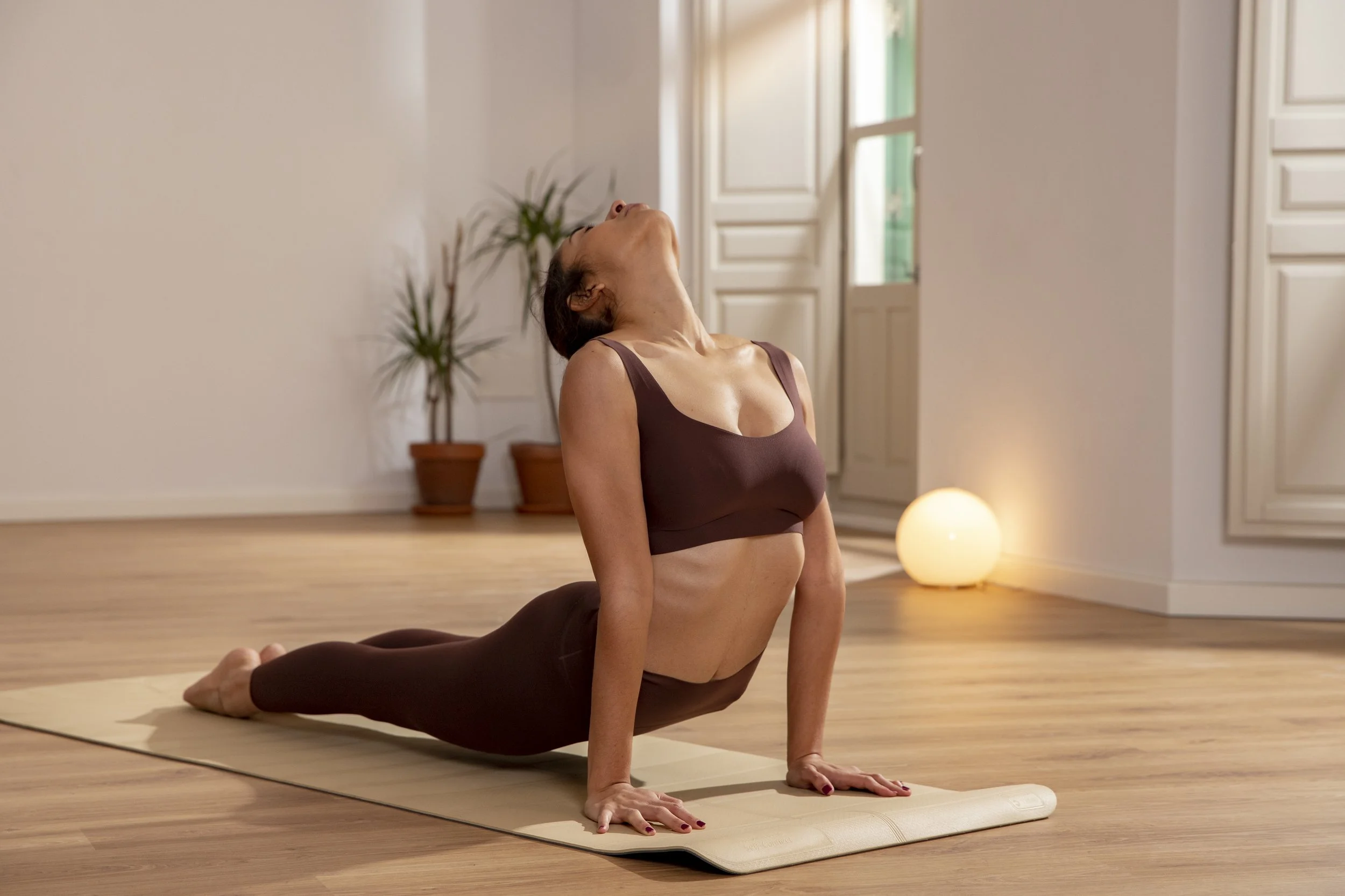 Woman practicing yoga indoors, performing a backbend pose on a yoga mat.