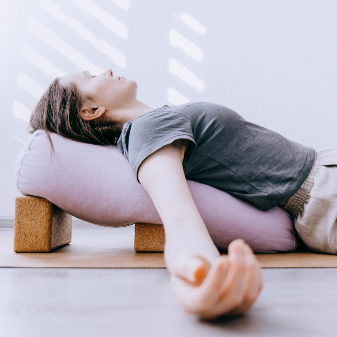 Person lying on a yoga prop with a cushion under their back, practicing relaxation or yoga.