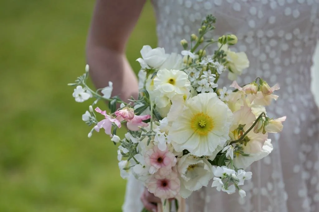 A bride holding a bouquet of various white and pink flowers outdoors.