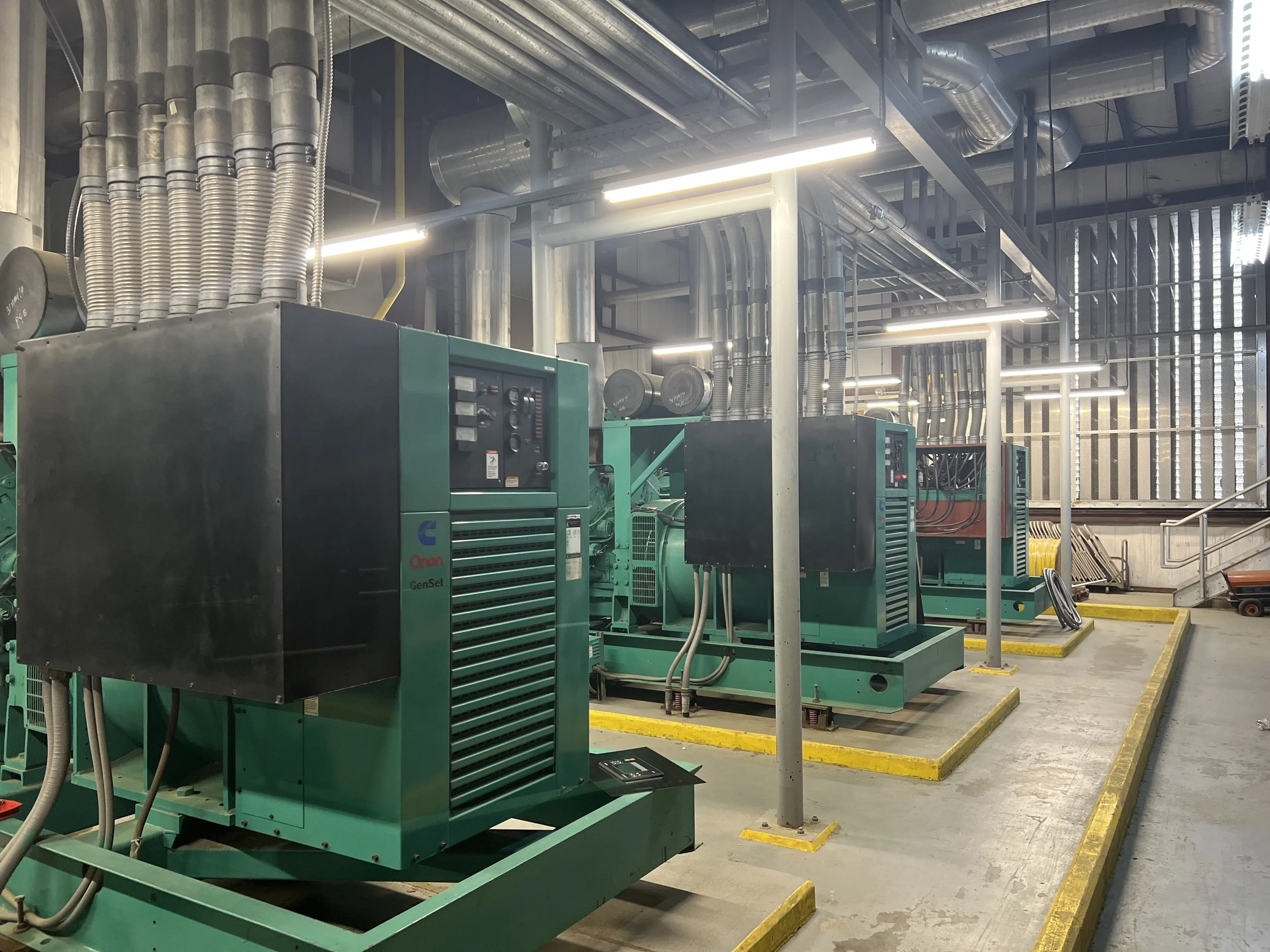 Industrial setting with multiple large Onan GenSet generators, metal piping, and ventilation ducts.