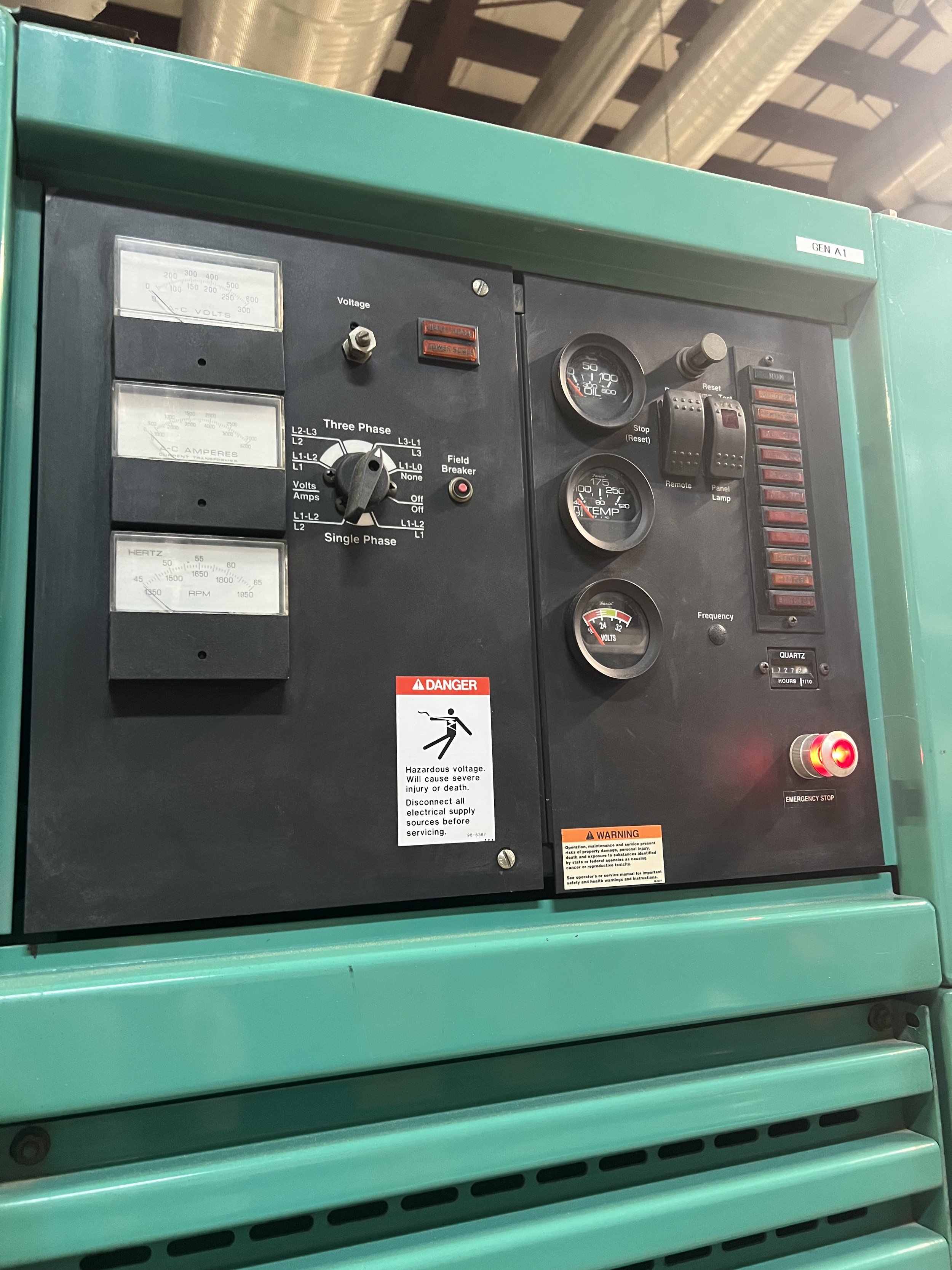 Industrial control panel with gauges, switches, warning labels, and an emergency stop button.