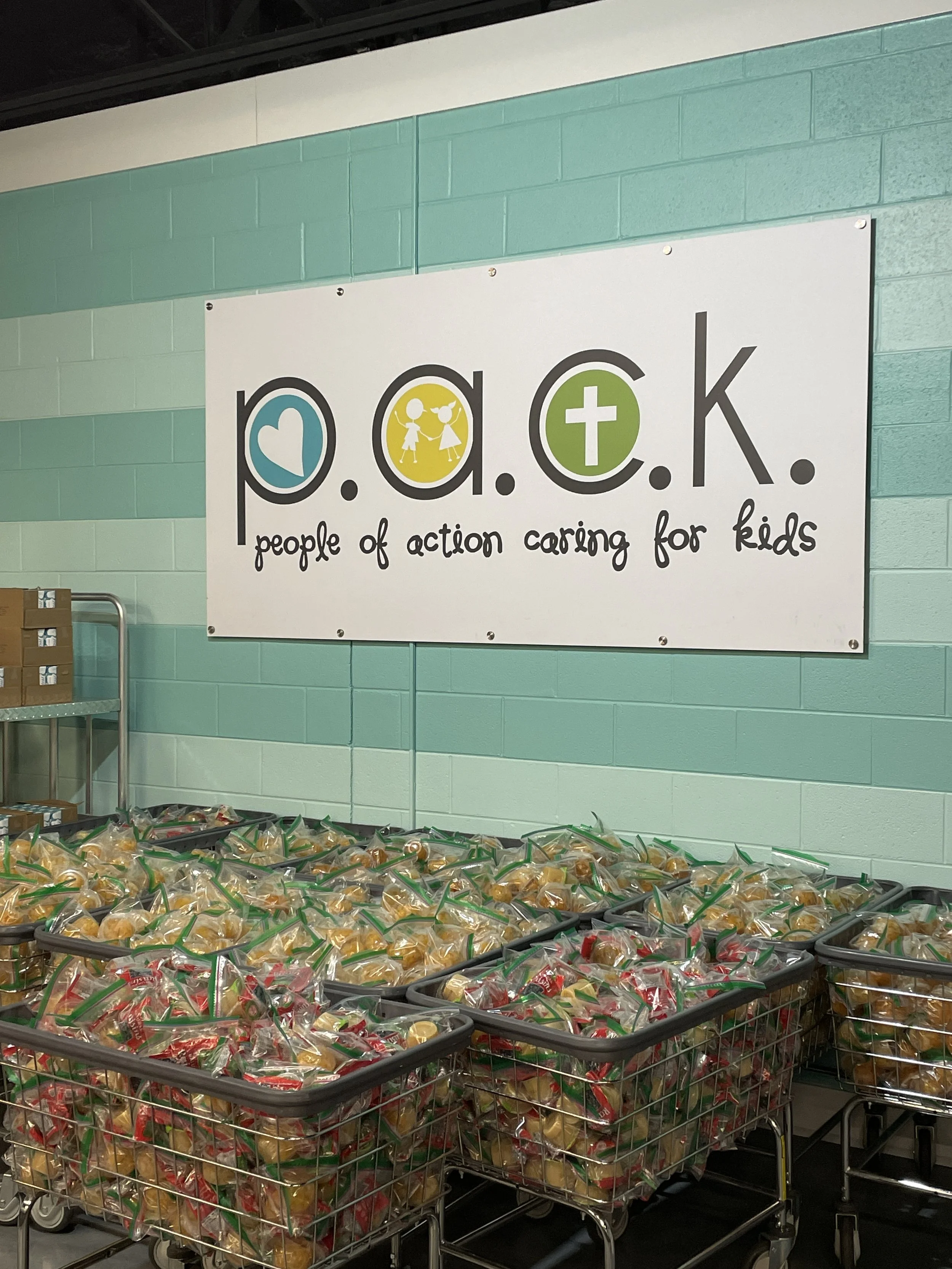 Baskets filled with snacks in front of a sign that reads 'P.O.C.K. people of action caring for kids' with icons of a heart, children, and a cross.