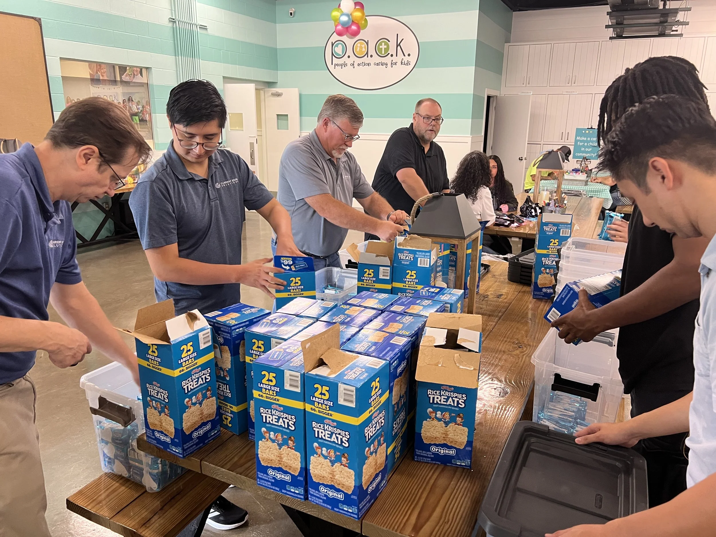 People packing boxes of Rice Krispies Treats at a community event with a 'People of Action' sign in the background.