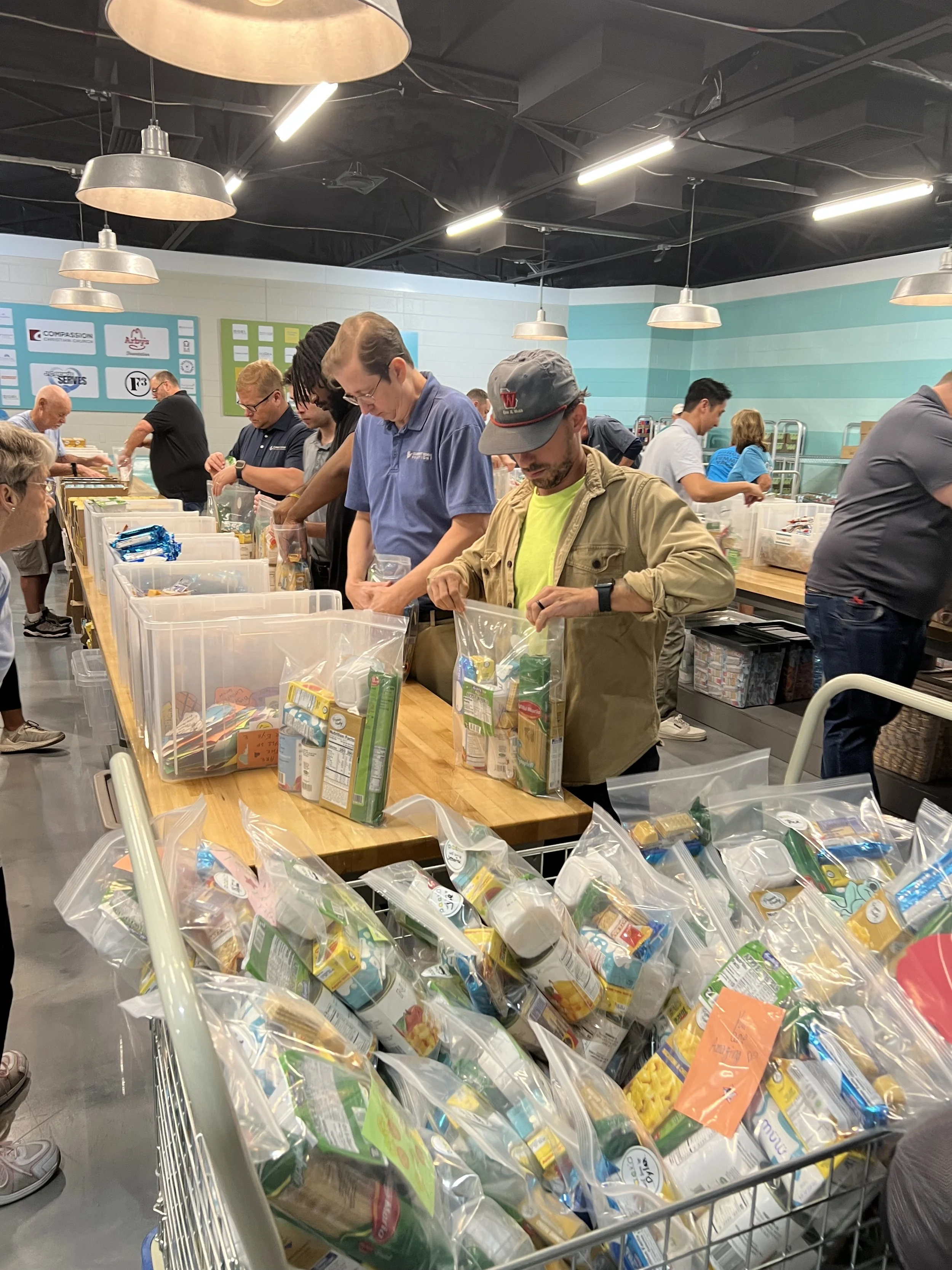 People packing food items into plastic bags at a food bank or donation center.