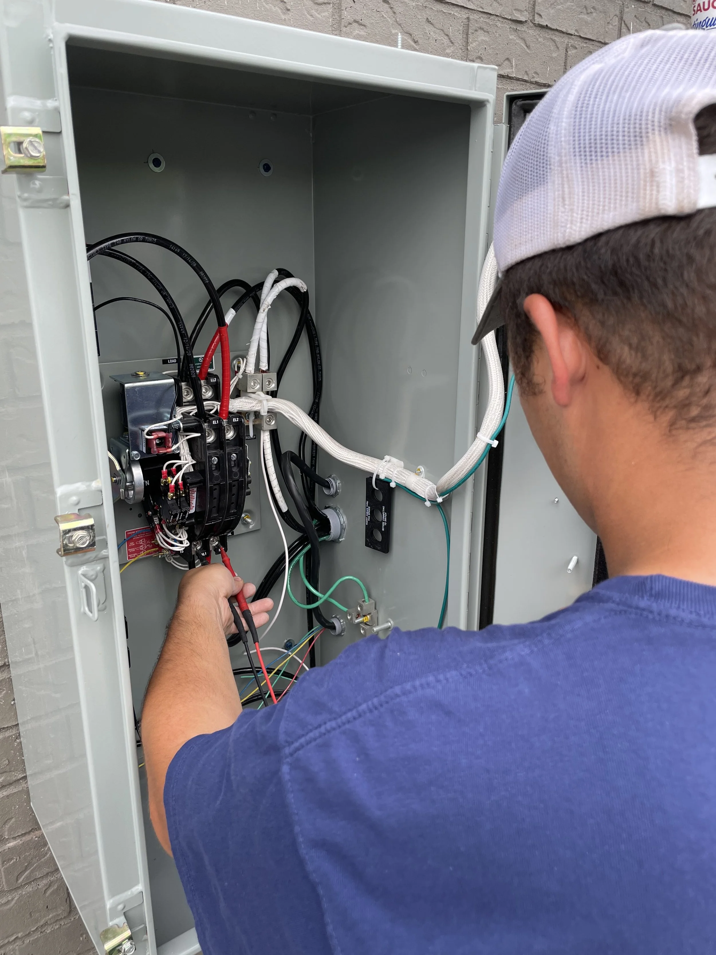 A man working inside an electrical panel outdoors with exposed wires and electrical components.