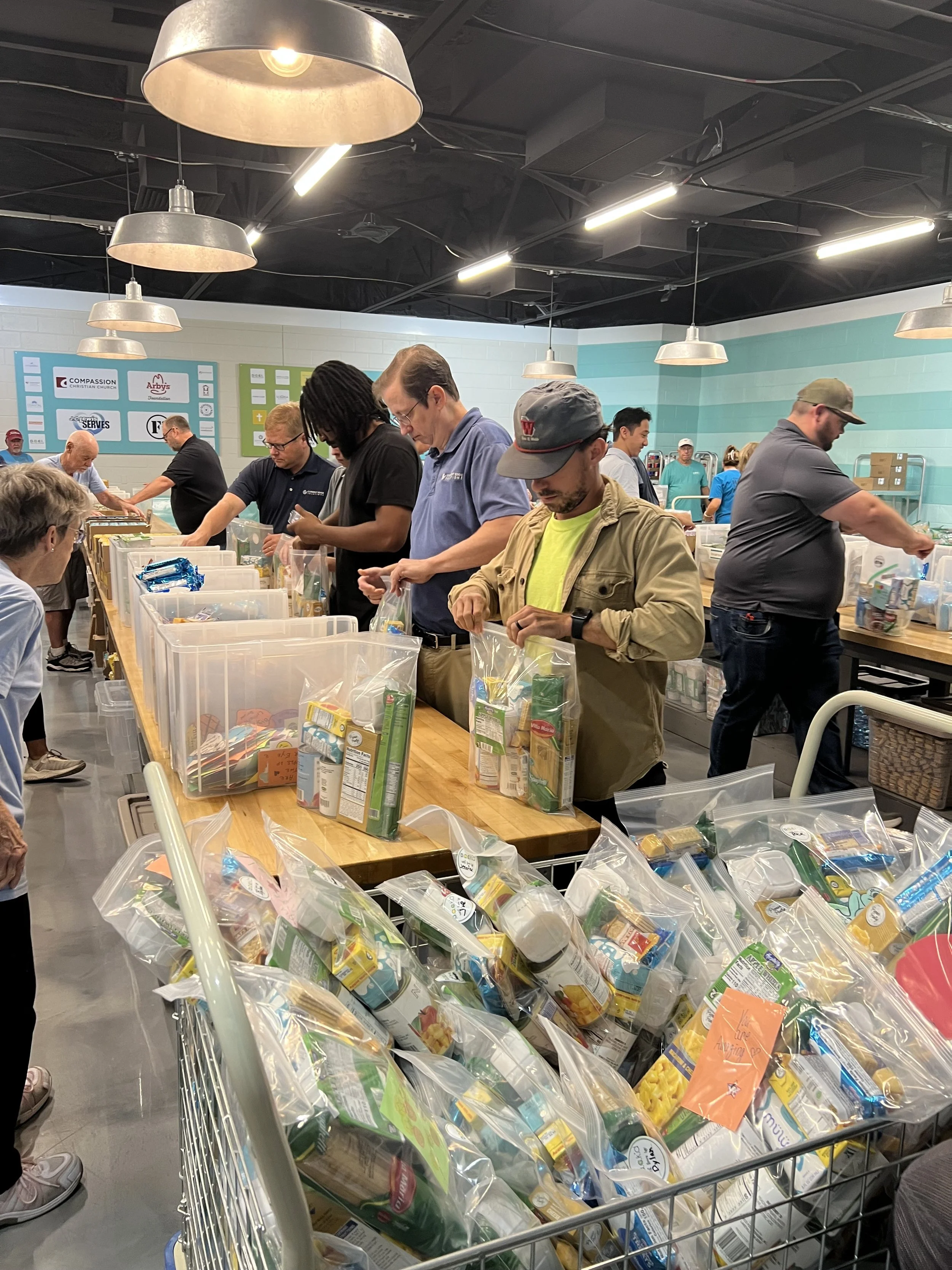 People packing food items into plastic bags at a community food bank or packing event.