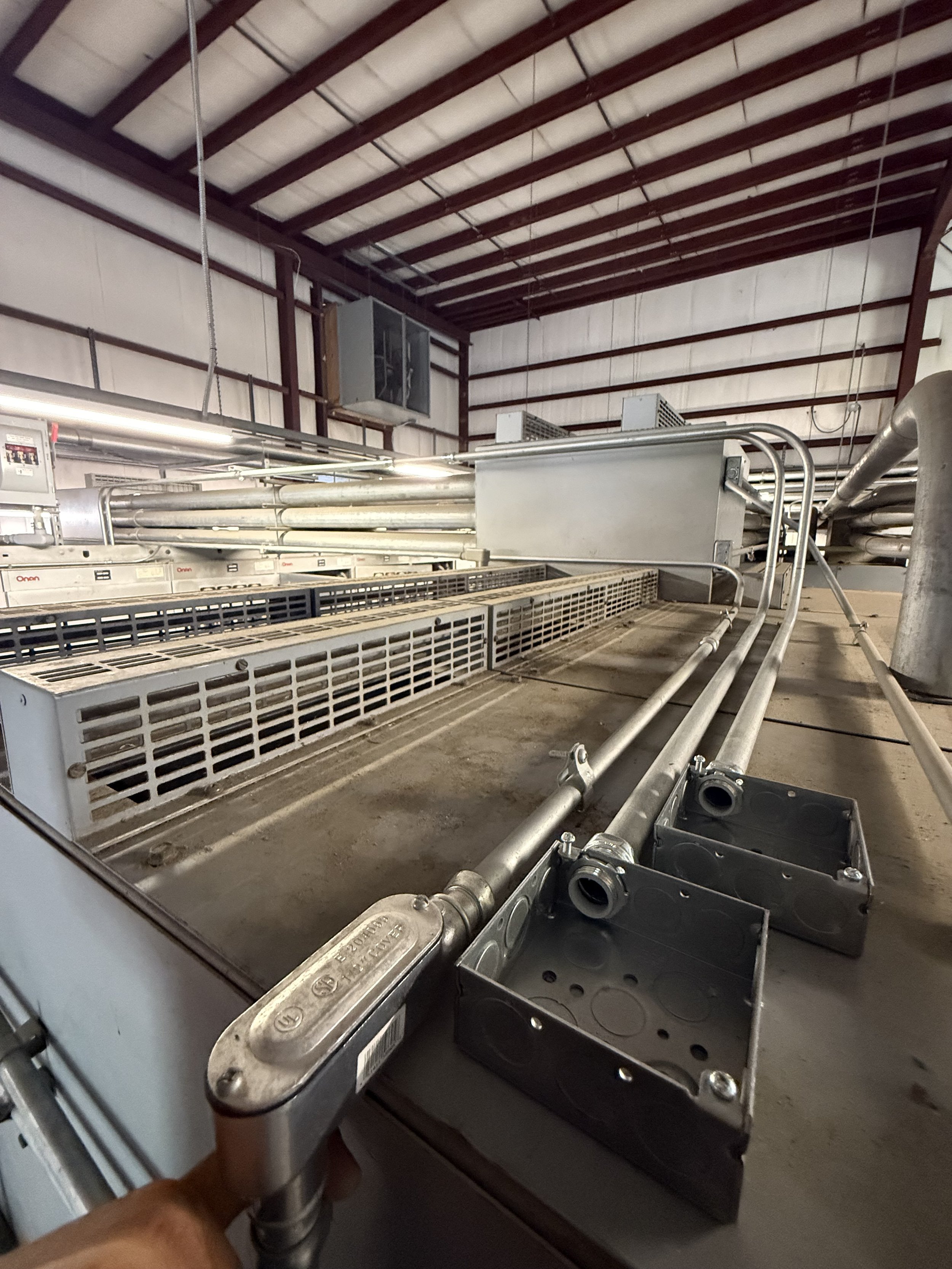 Interior of a warehouse or industrial facility with metal pipes, electrical panels, and ventilation units.