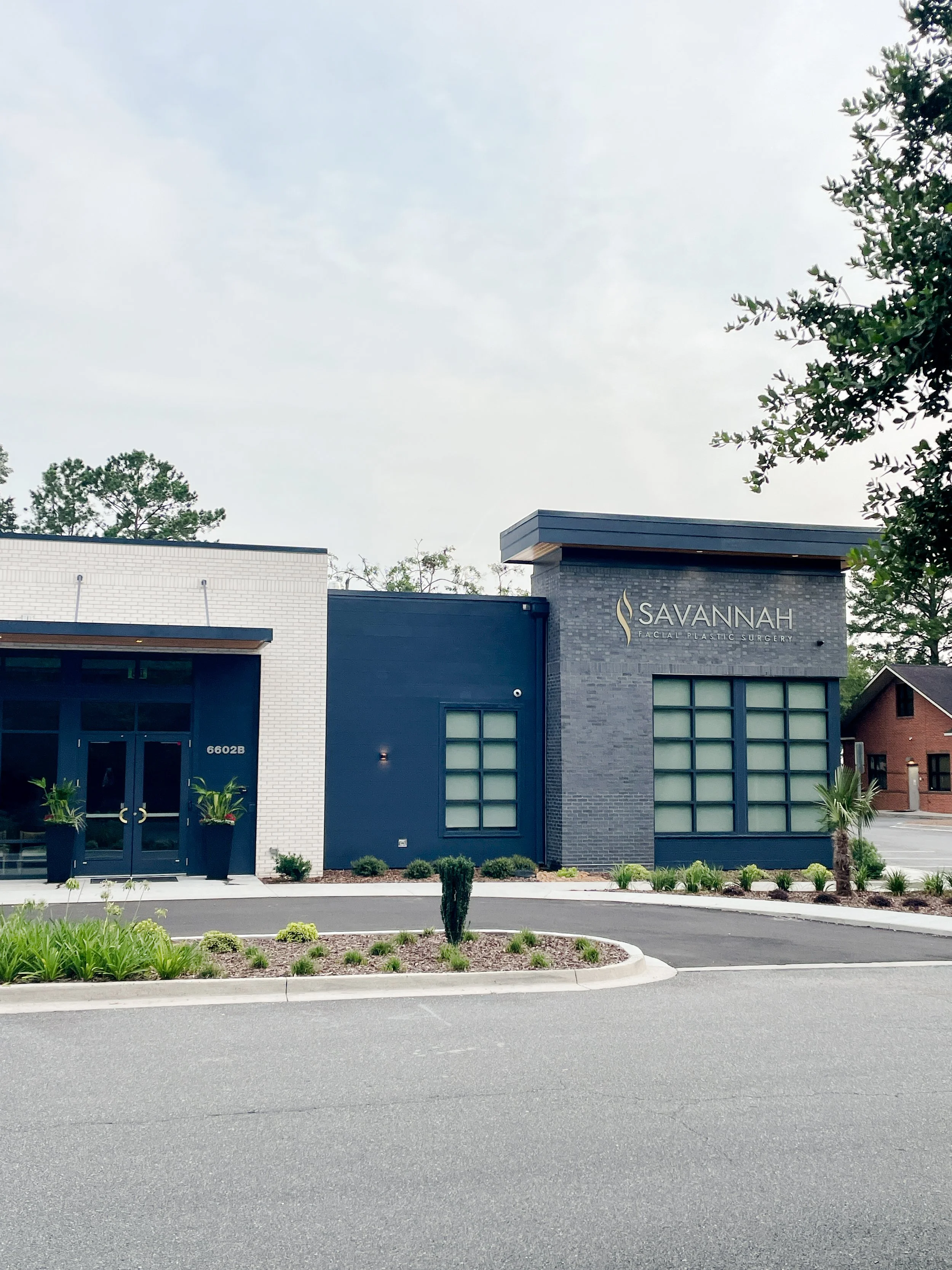 Exterior view of Savannah Facial & Plastic Surgery building with modern black and white facade, large windows, and landscaped front yard.
