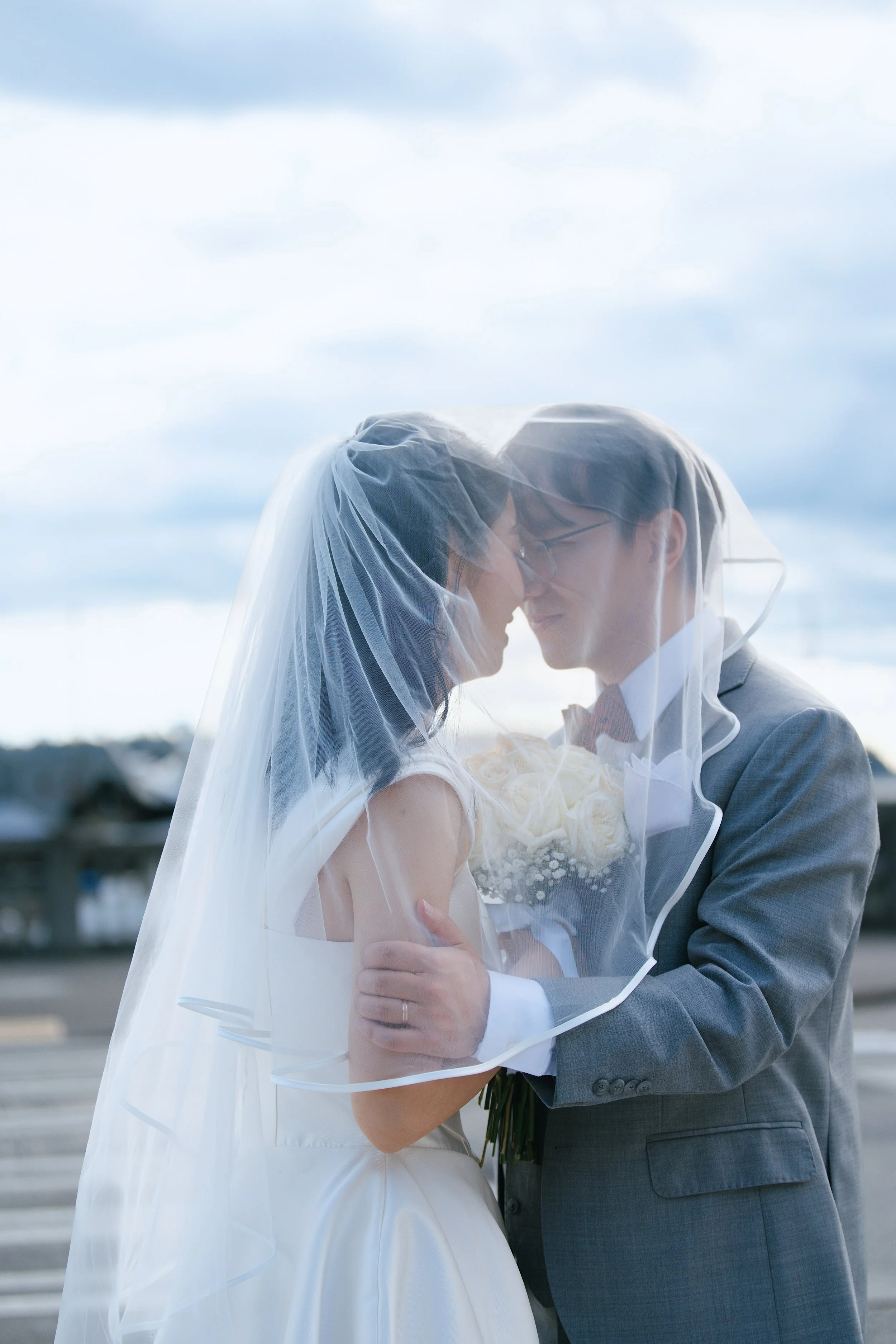 Newlywed couple kissing beneath the bride’s veil outdoors