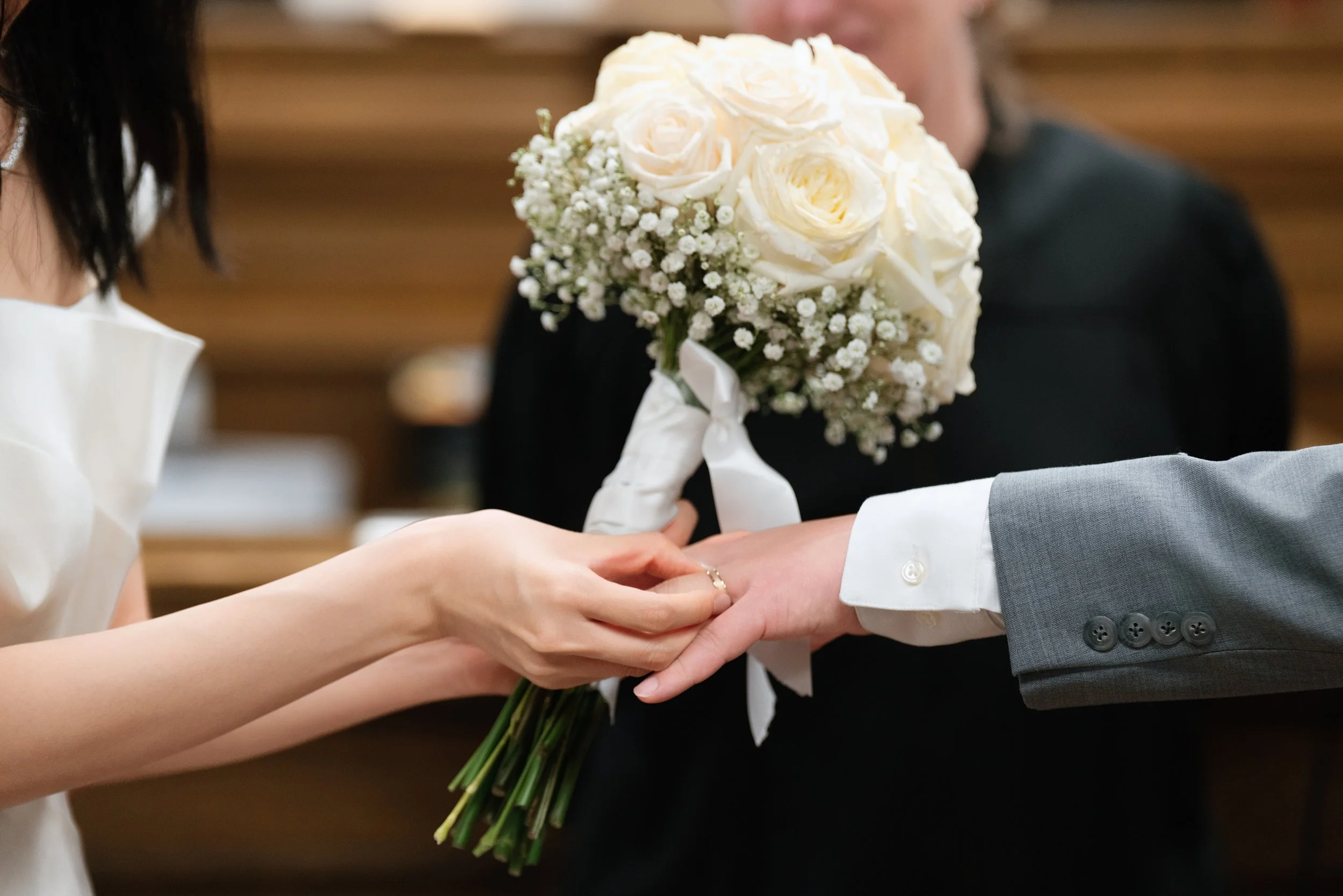 Couple exchanging wedding rings beside a white rose and baby's breath bouquet