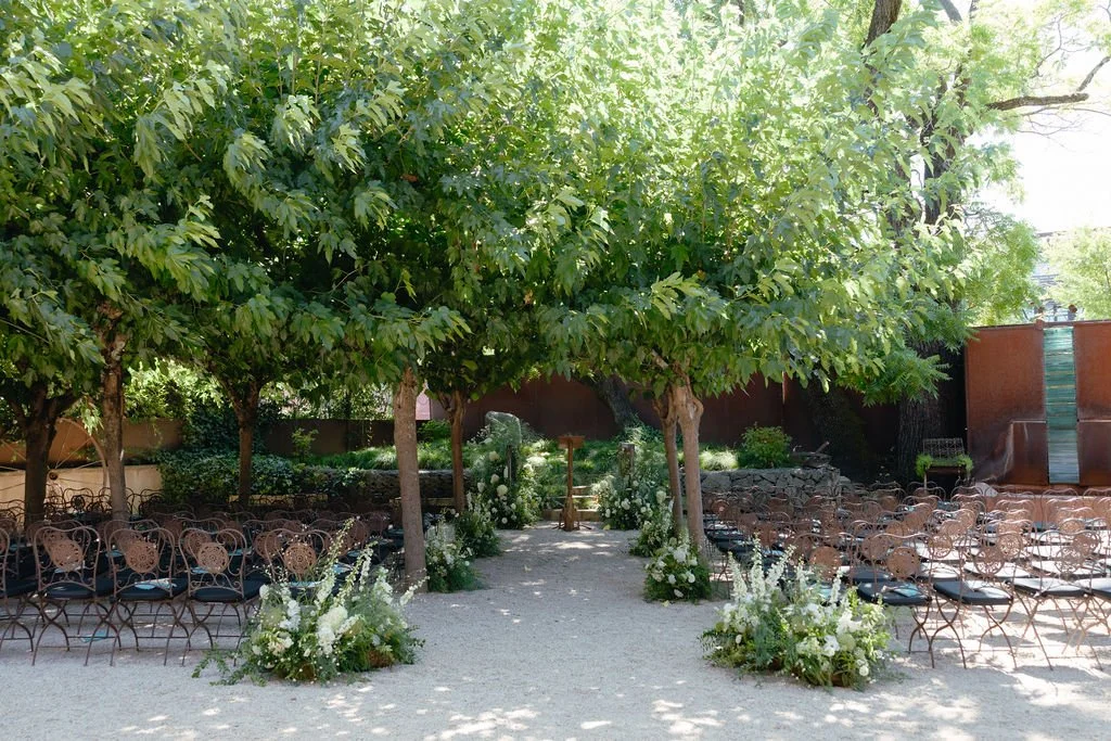 Outdoor wedding ceremony setup with rows of chairs, aisle floral arrangements, a pathway, and a large leafy tree providing shade in Healdsburg, CA