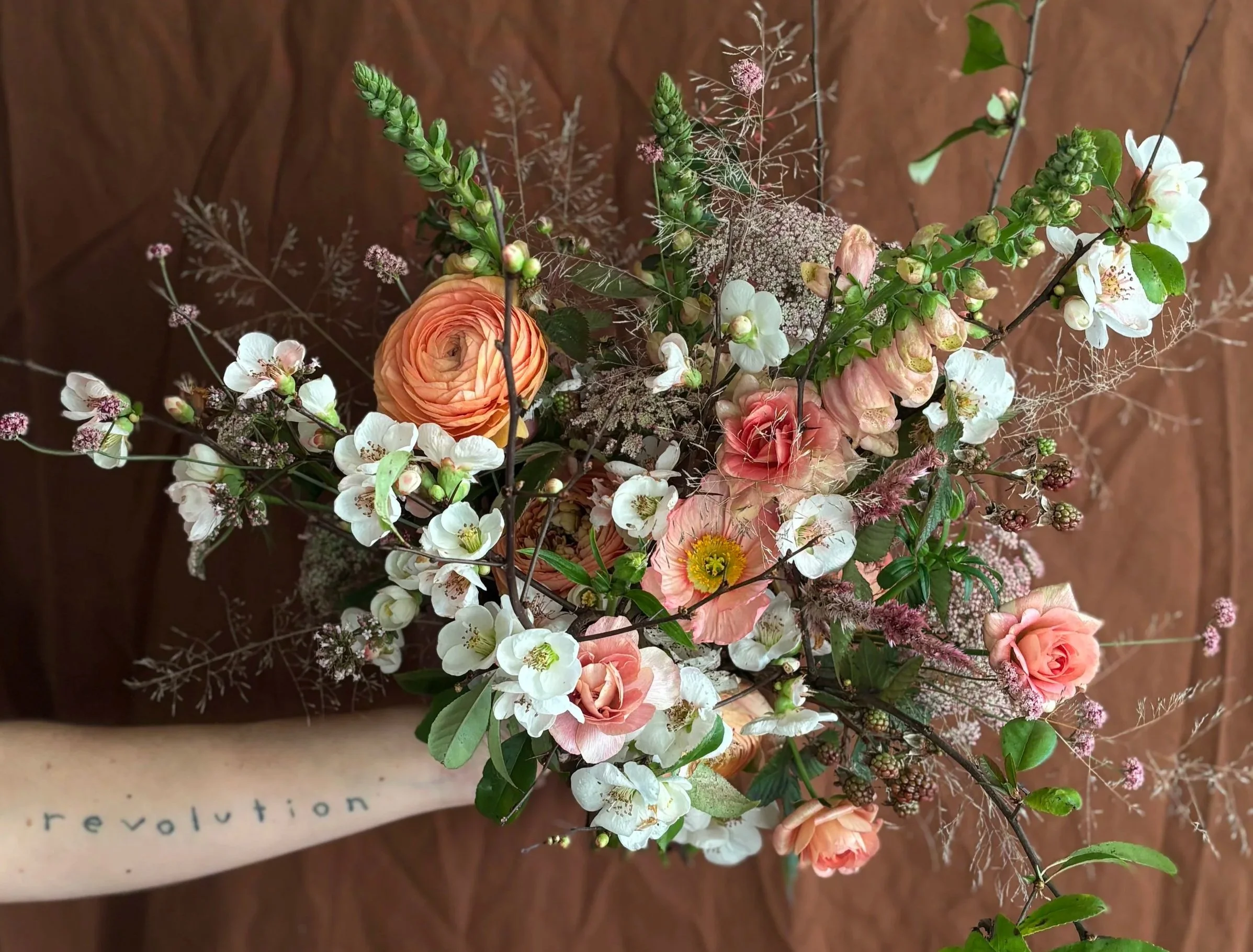 Close up of bridal bouquet with ranunculus, quince blossoms, foxgloves, poppies and foliage.