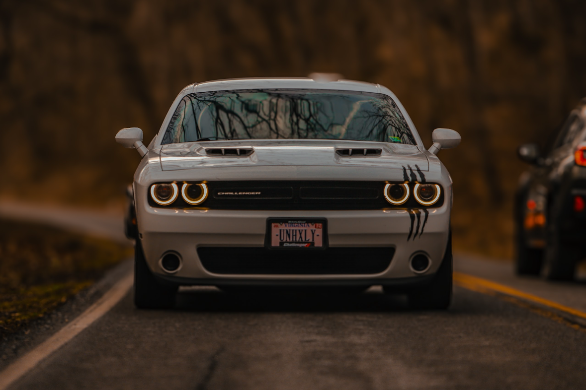 A white Dodge Challenger parked on a winding road with a blurred natural background.