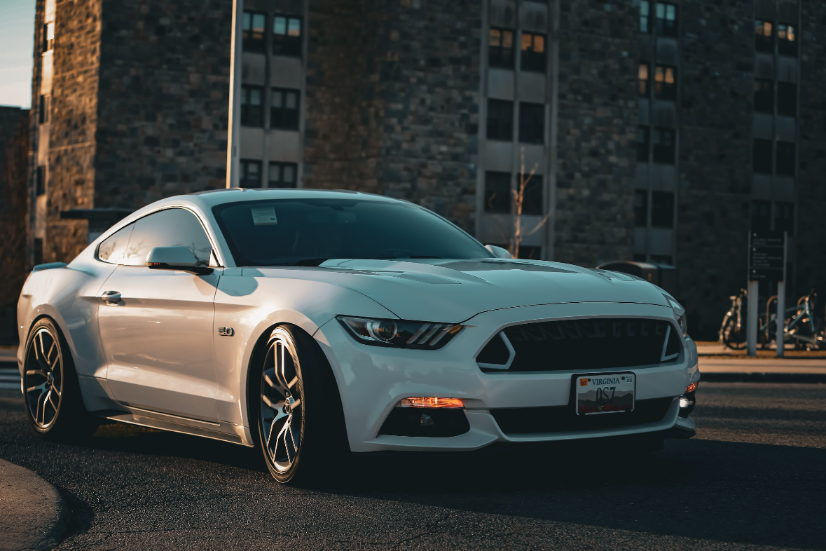 White Ford Mustang parked on city street during sunset with tall buildings in the background.