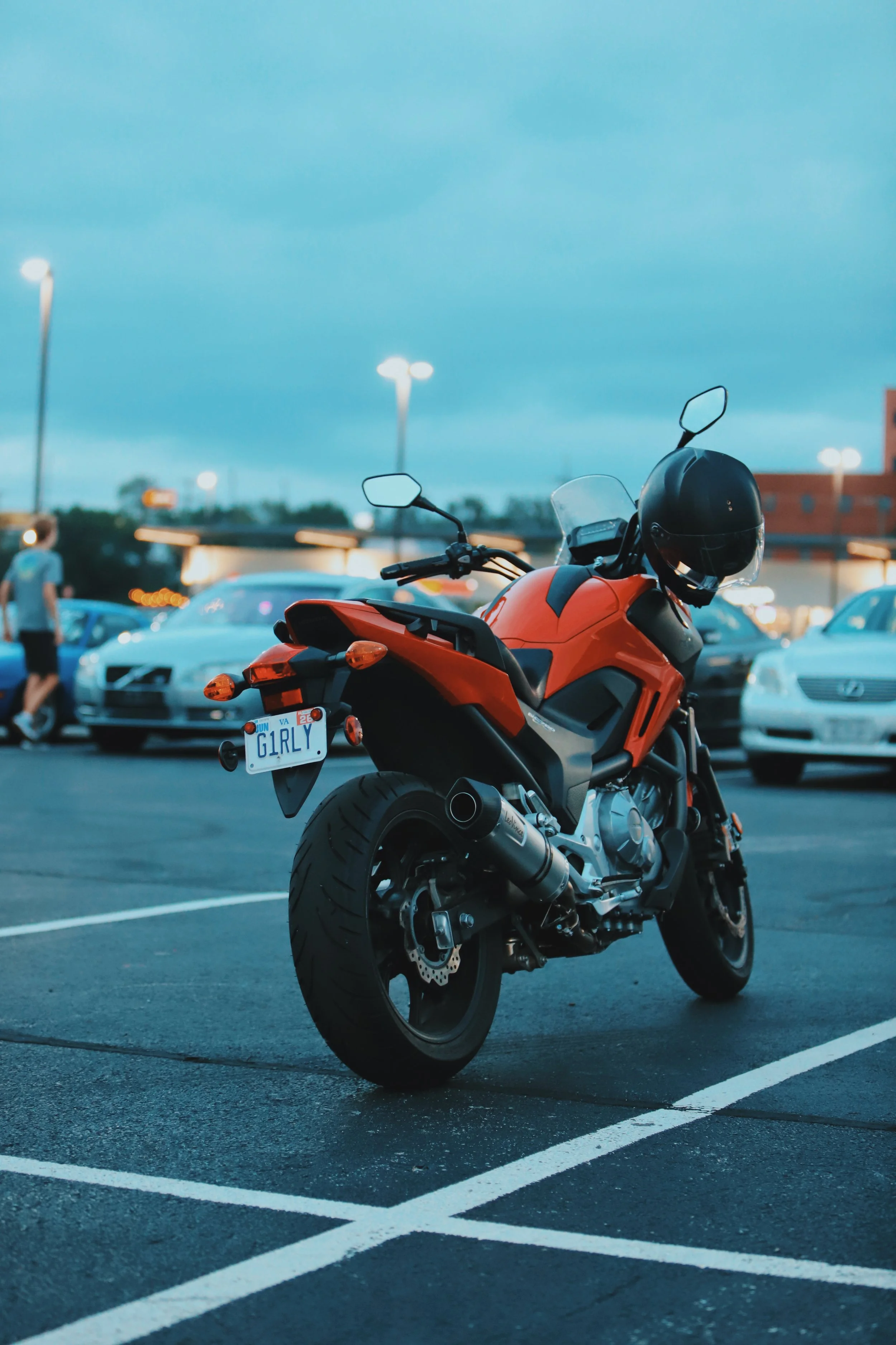 An orange motorcycle parked in a parking lot at dusk.