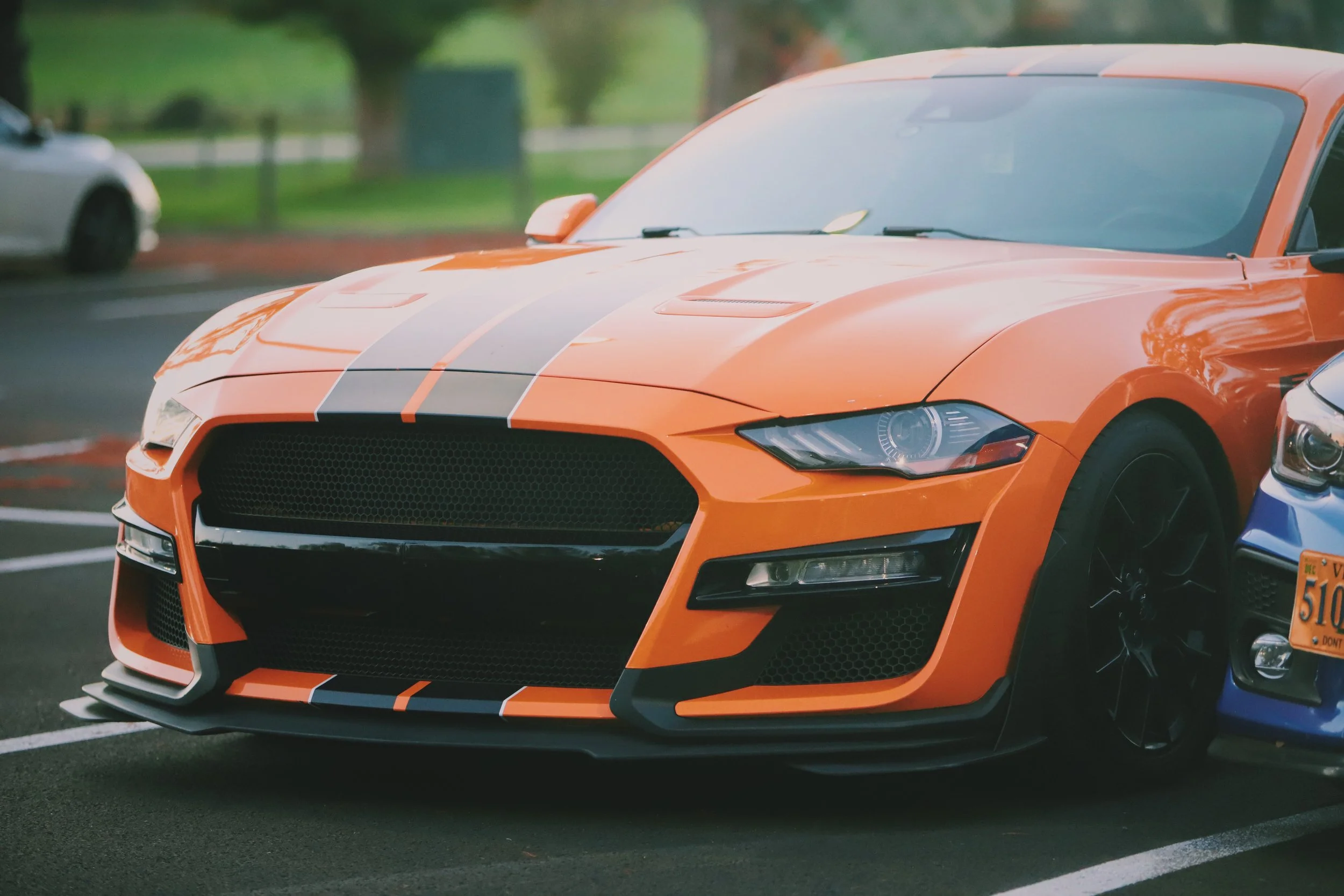 Orange sports car with black racing stripes parked in a parking lot at dusk.