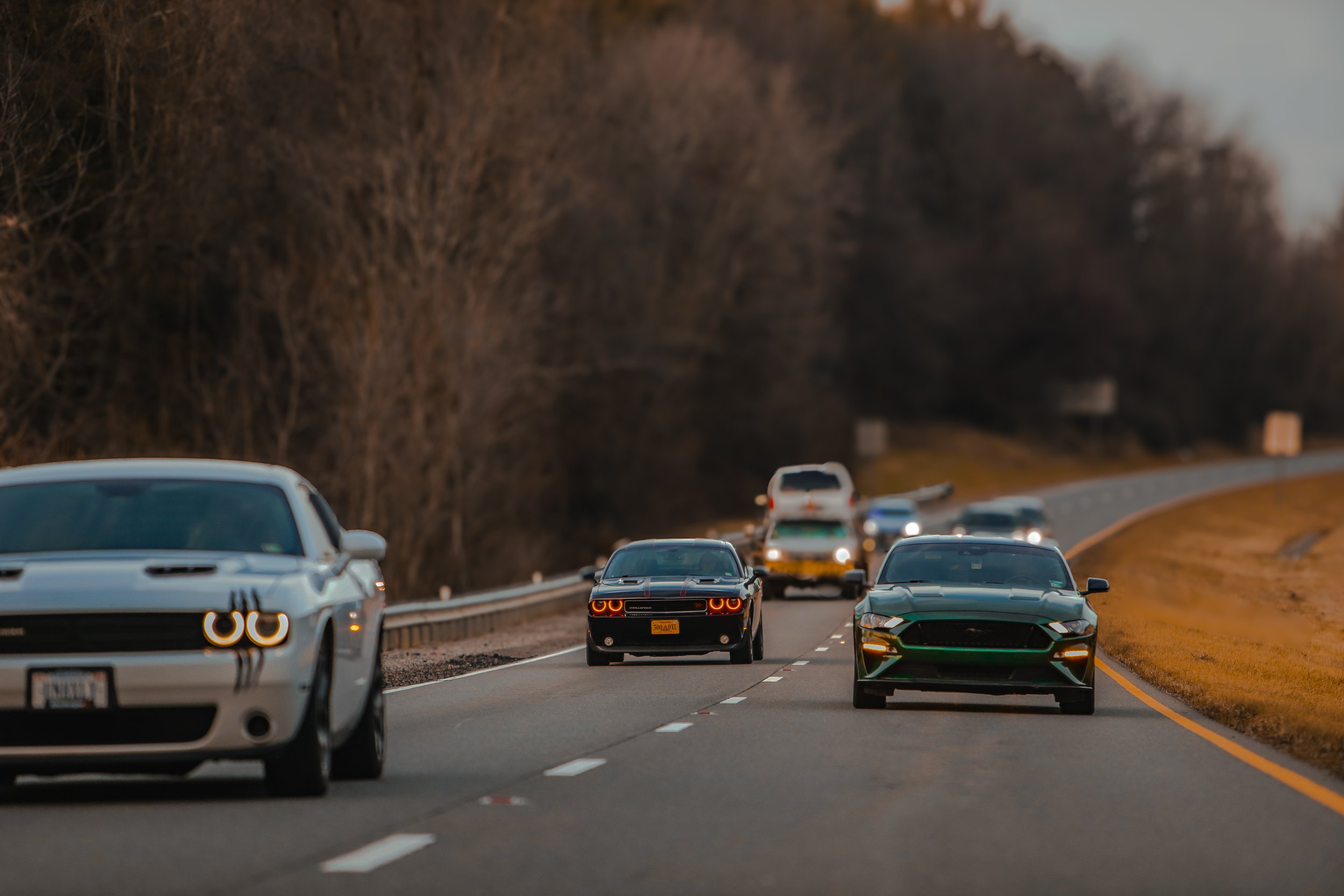 Multiple cars driving on a winding highway, with a forested area on both sides, during daytime.