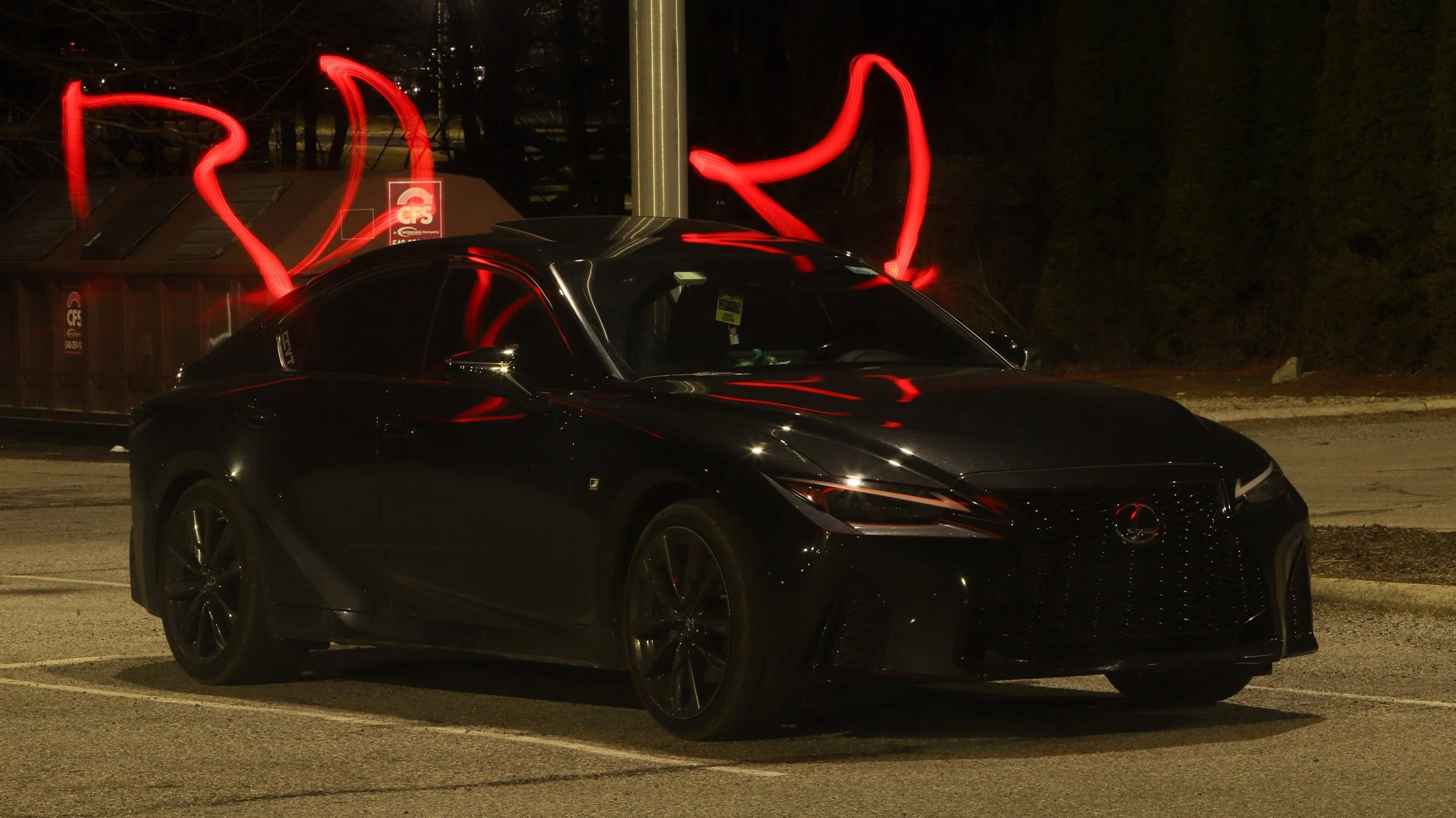 Black Mazda sedan parked at night with red light streaks swirling behind it, possibly from a light source moved during long exposure photography.