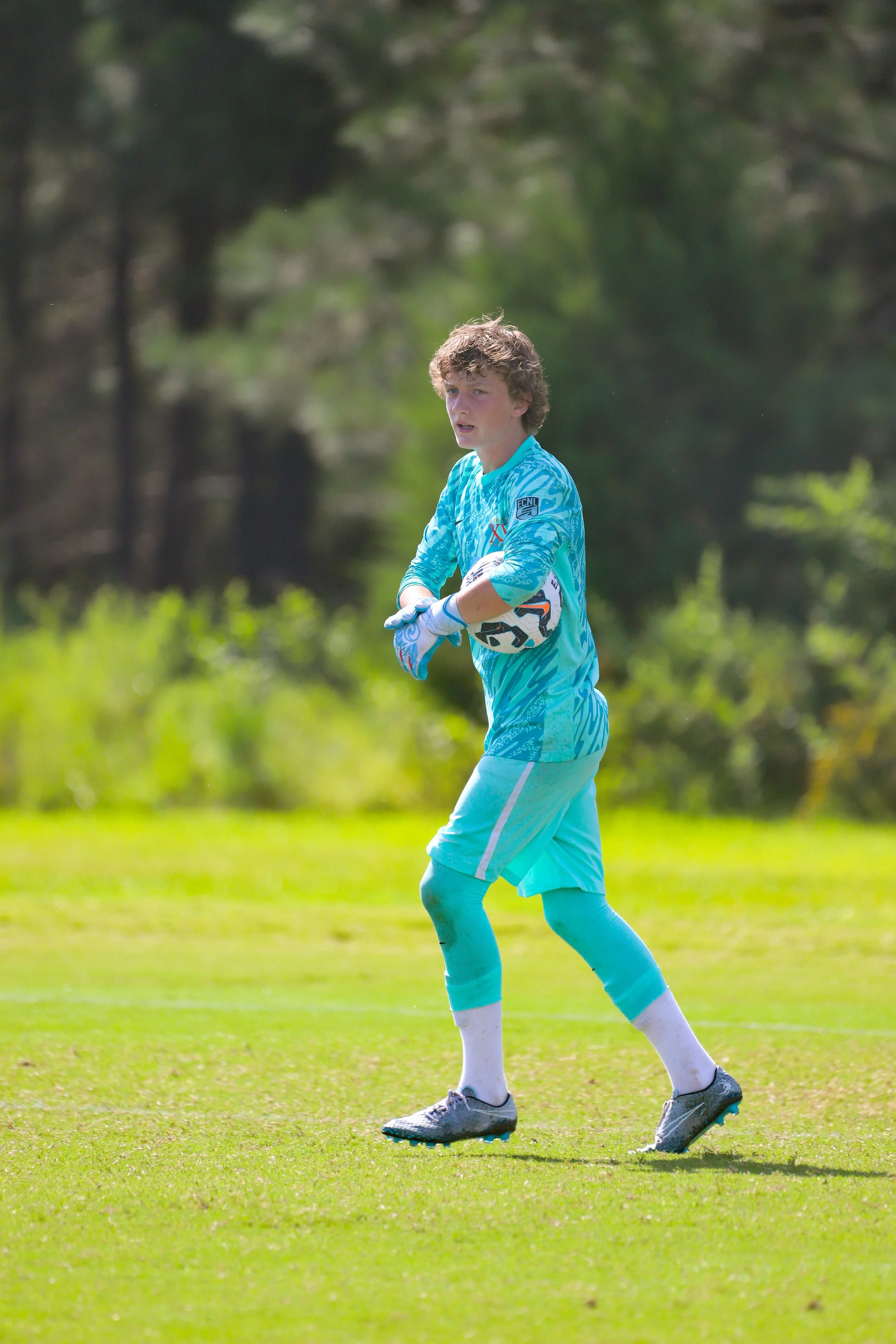 A young boy dressed as a soccer goalkeeper holding a soccer ball on a grassy field.