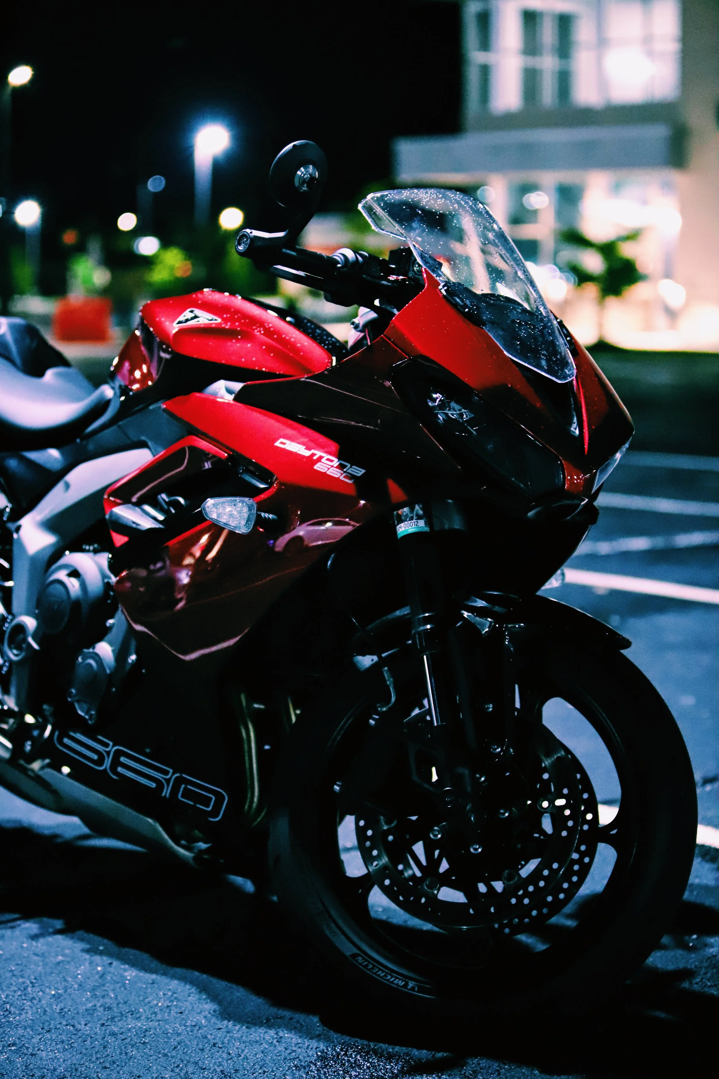 A red and black Ducati Panigale V4 motorcycle parked in a lot at night, with wet rain drops on its windshield.